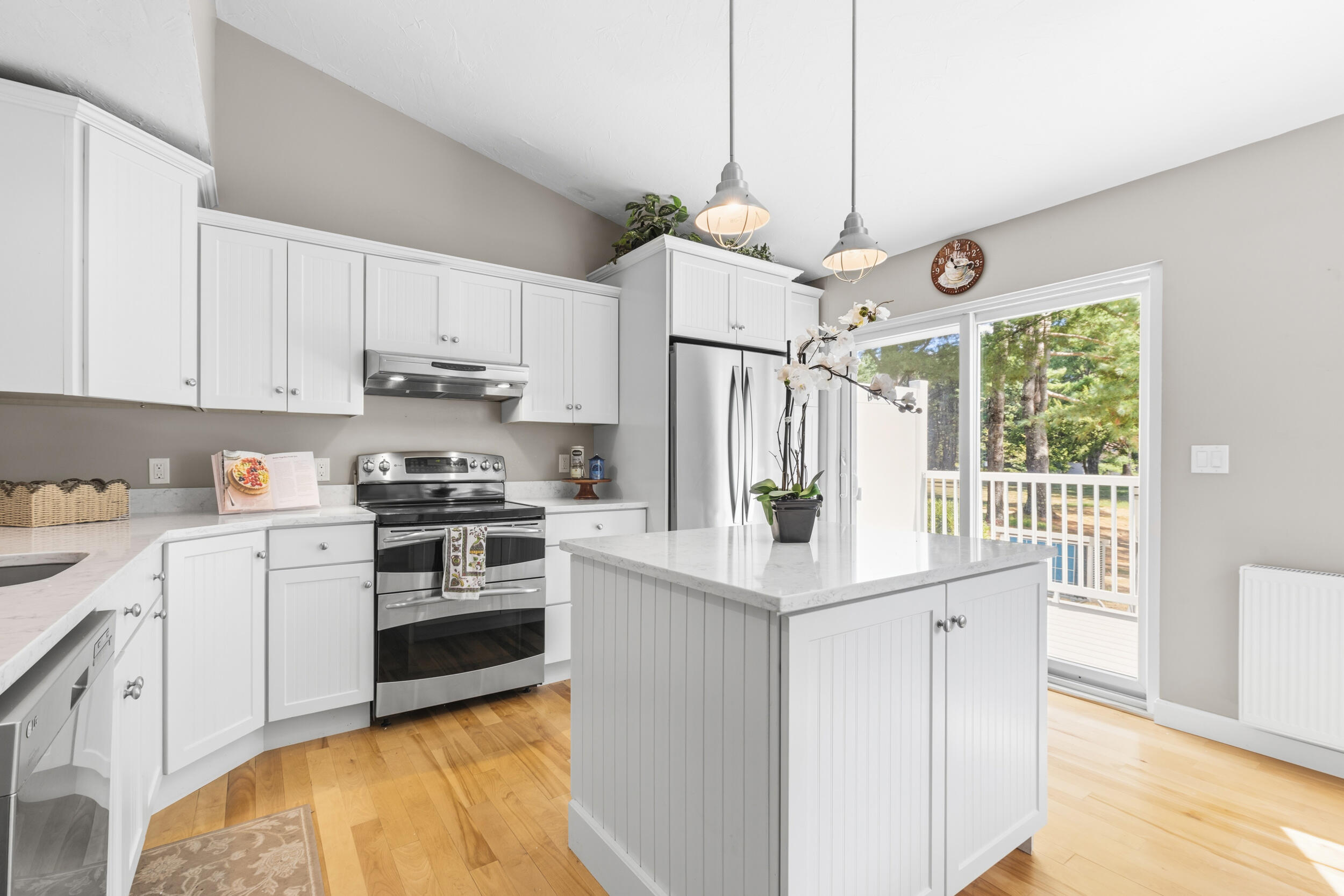 Bright kitchen with white cabinets, stainless appliances, a large island, and sliding doors to a tree-lined deck.