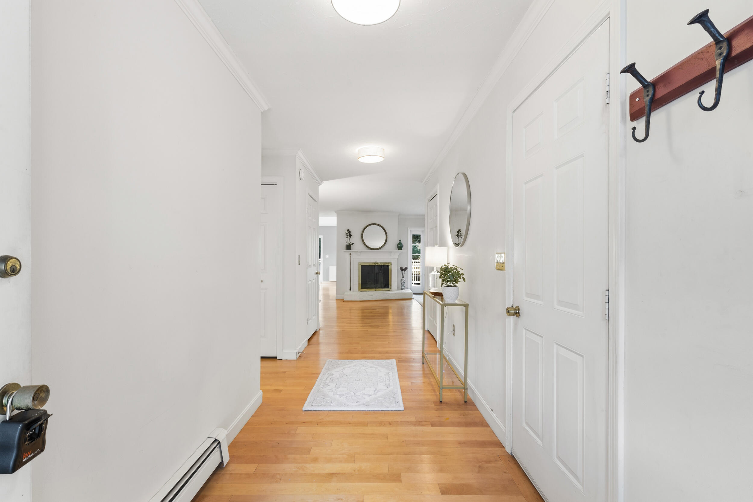 Bright hardwood hallway with white paneled doors, a console table, and a fireplace at the far end.