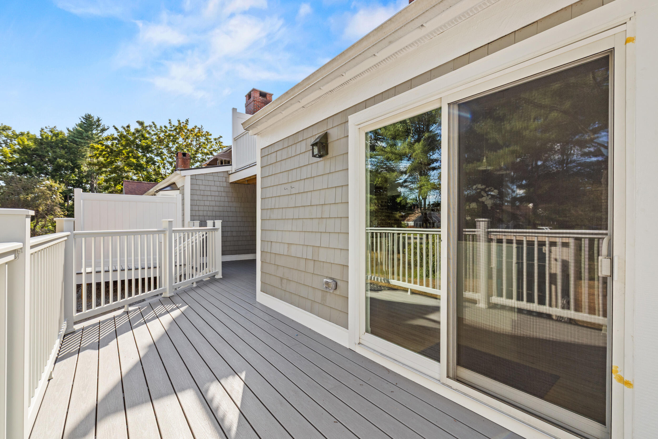 Outdoor deck with gray boards, white railings, and sliding glass doors.