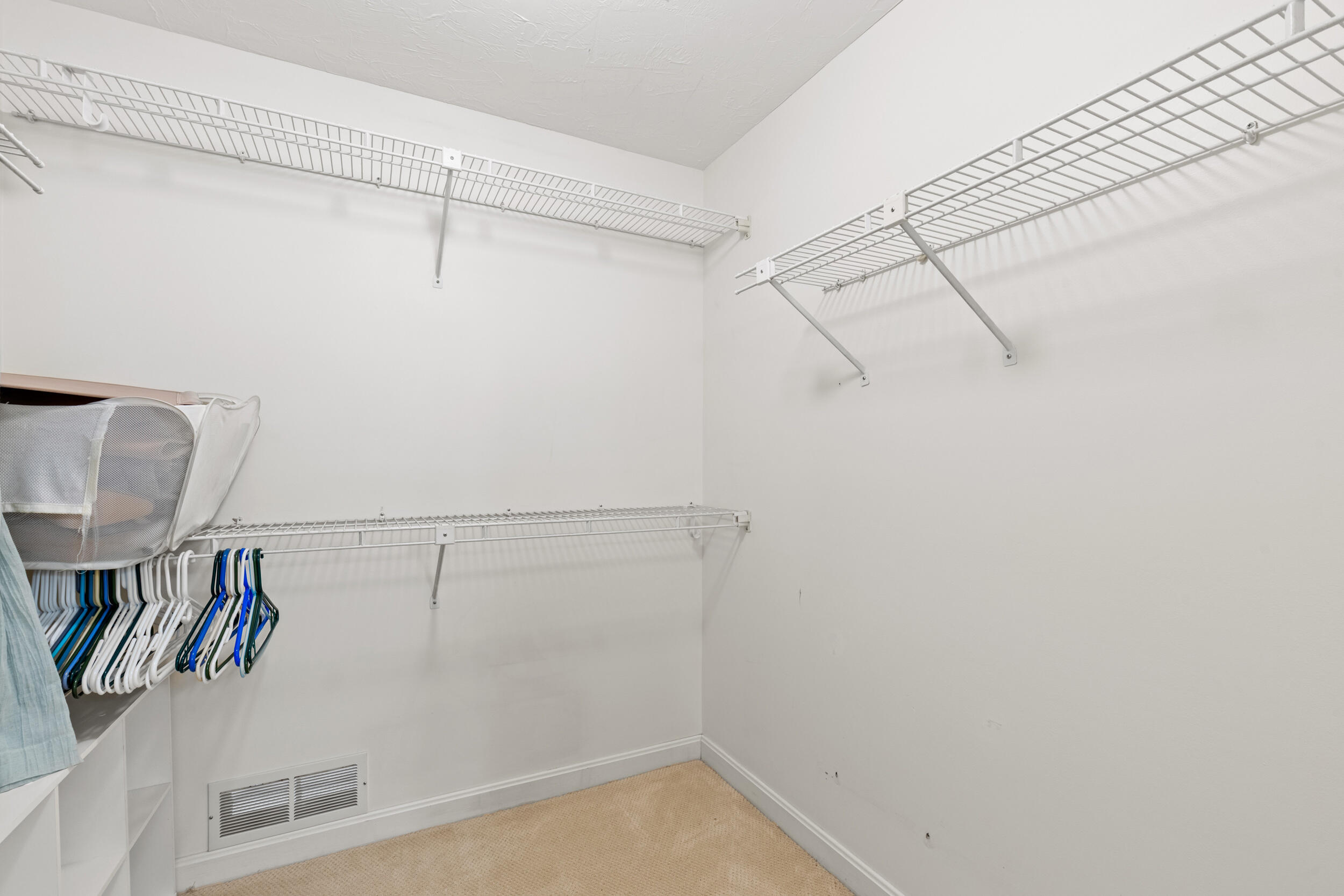 Walk-in closet with white wire shelving, built-in cubbies, and beige carpet.