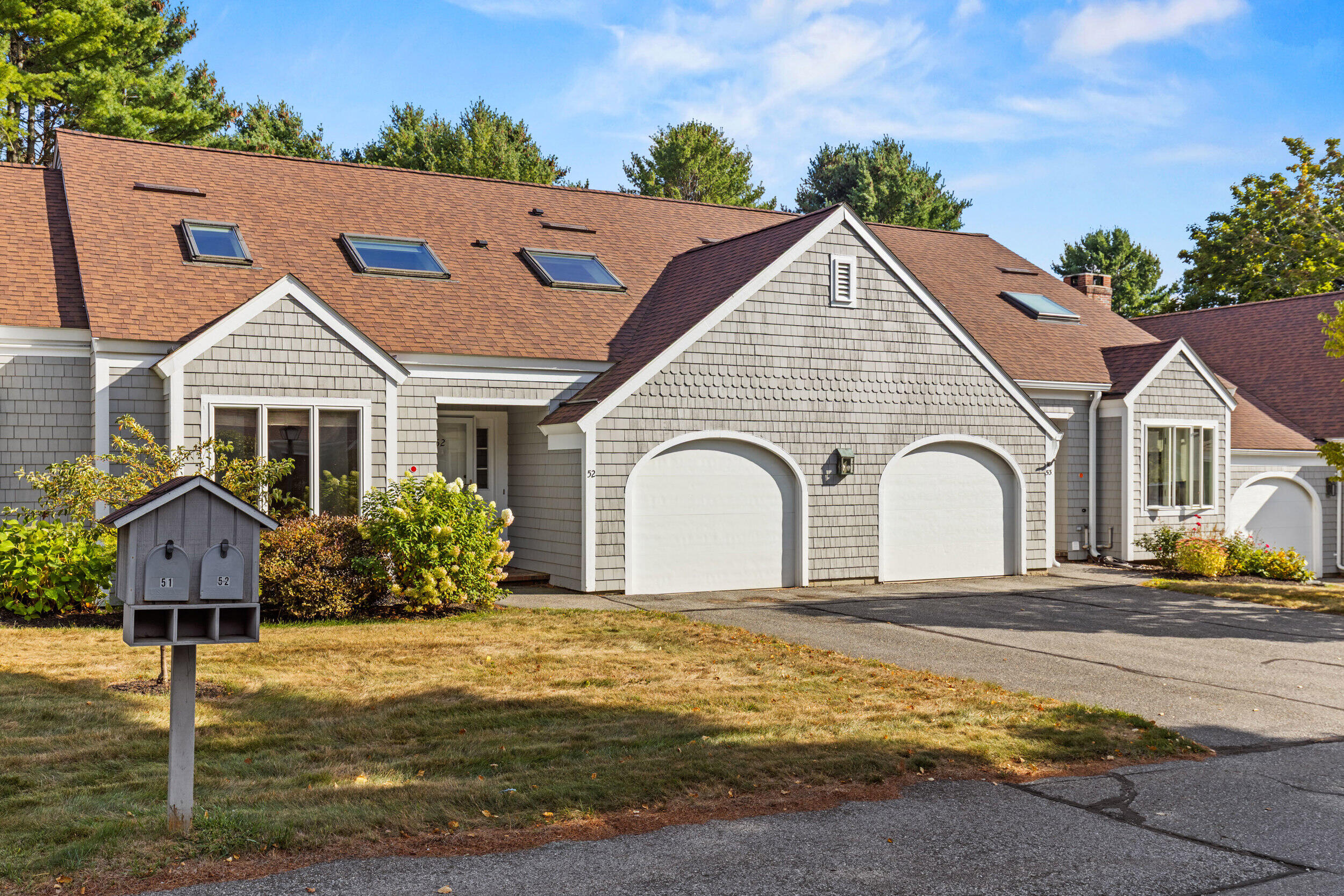 Gray shingle-sided home with two arched garage doors, roof skylights, and a mailbox marked 51 and 52.