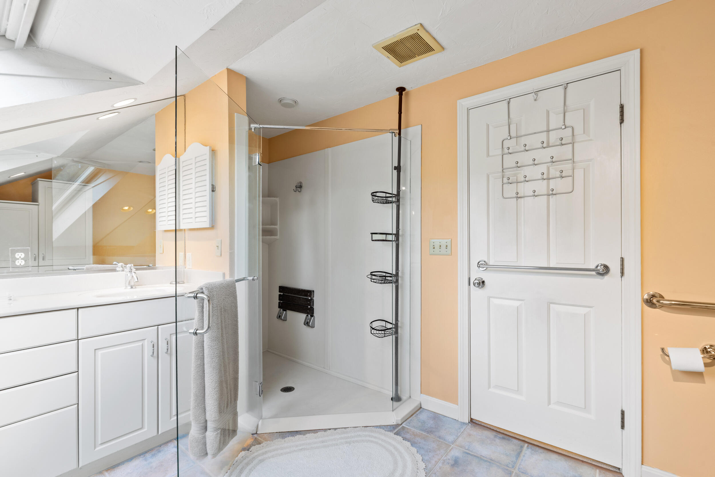 Bathroom with a glass walk-in shower, white vanity, peach walls, and grab bars.