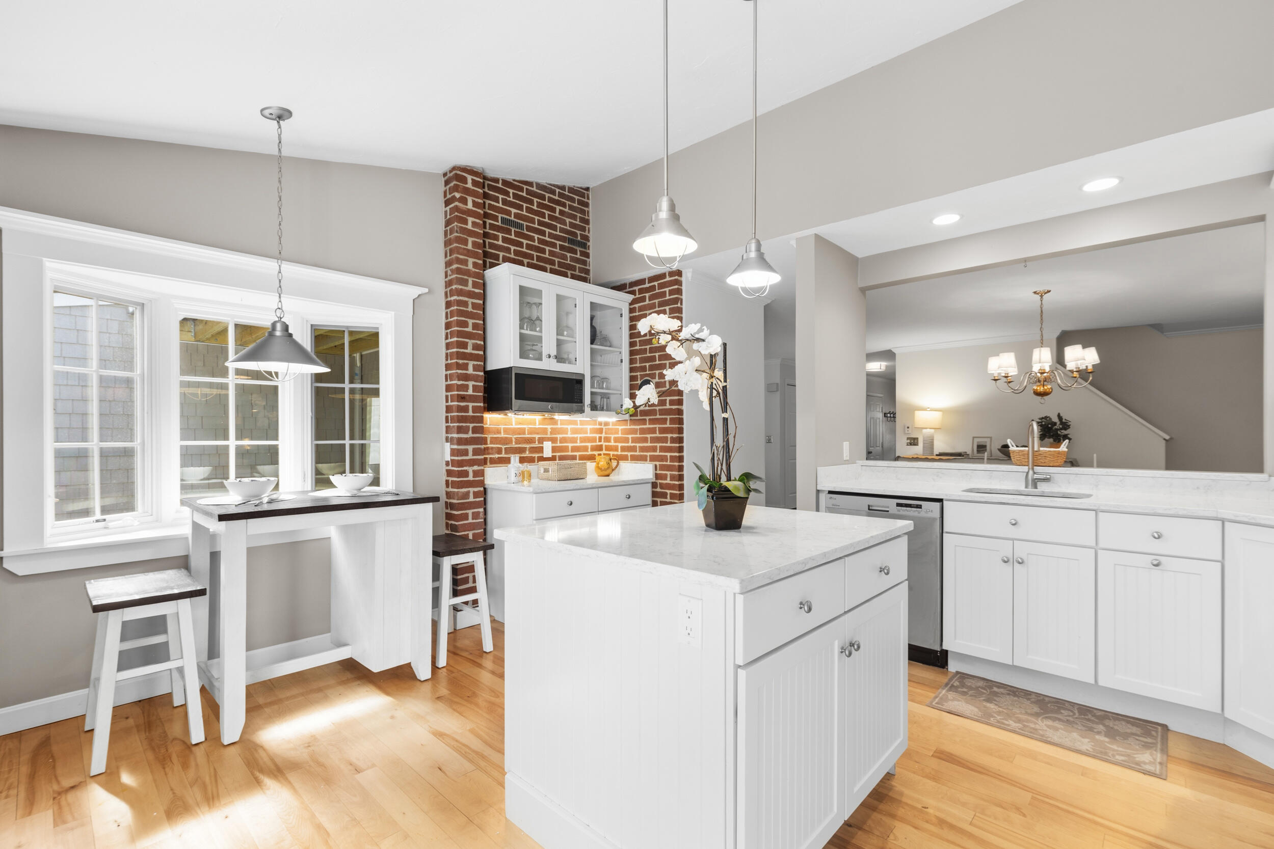 Bright kitchen with a large marble island, brick accent wall, and window-side breakfast bar.