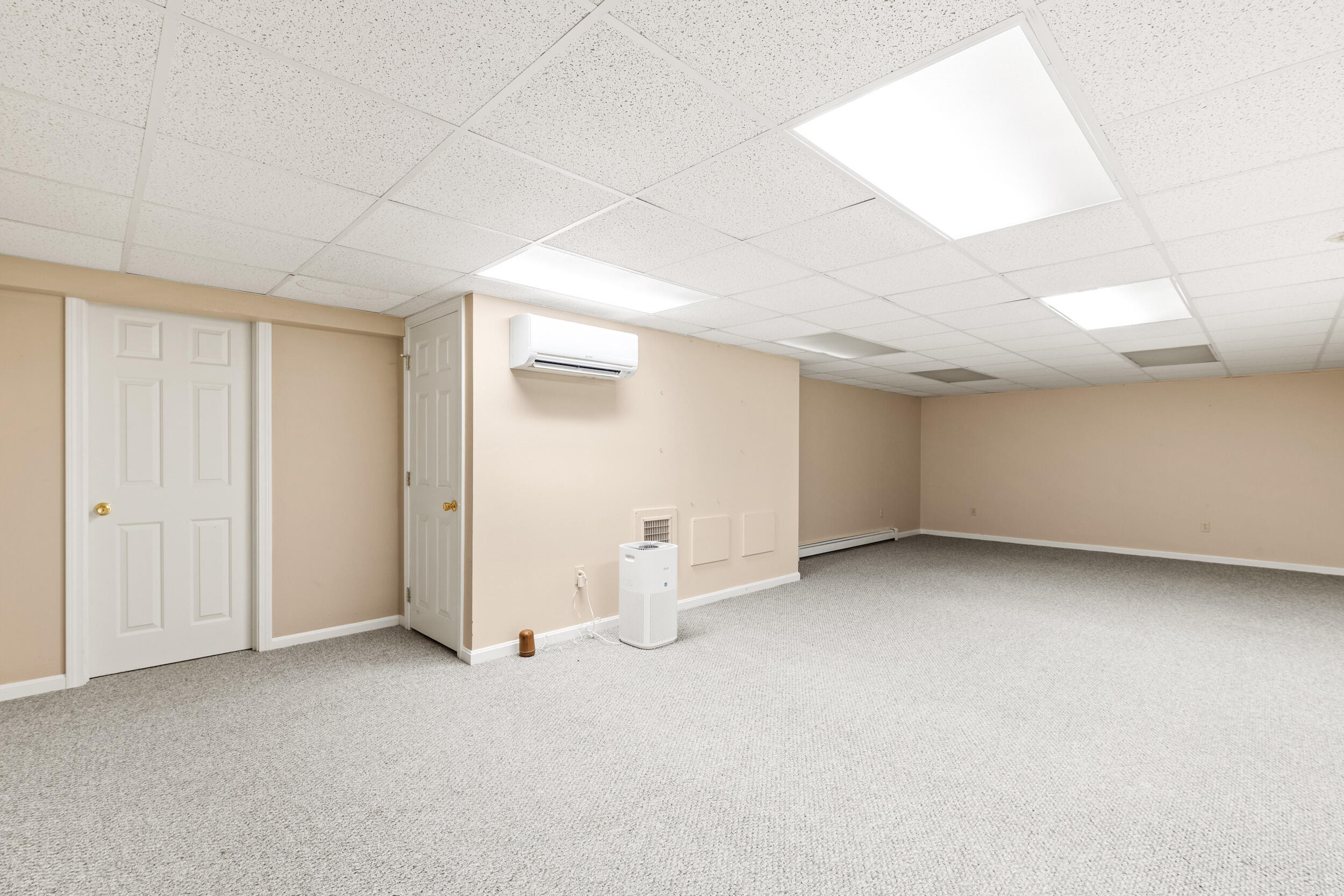 Empty carpeted room with beige walls, two white doors, and a wall-mounted mini-split air conditioner.