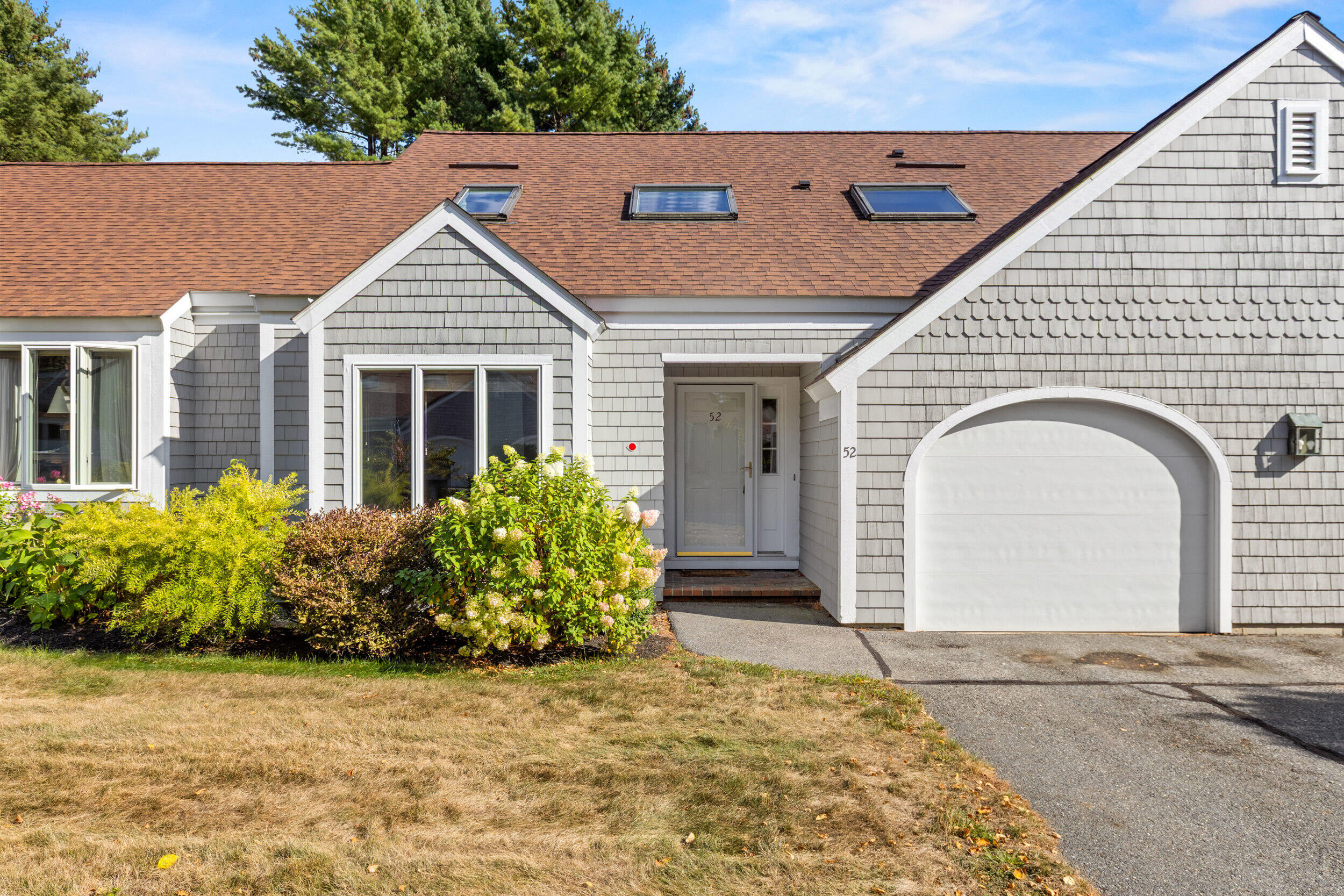 Gray shingle-sided home with an arched garage door, skylights, and shrubs by the entrance.