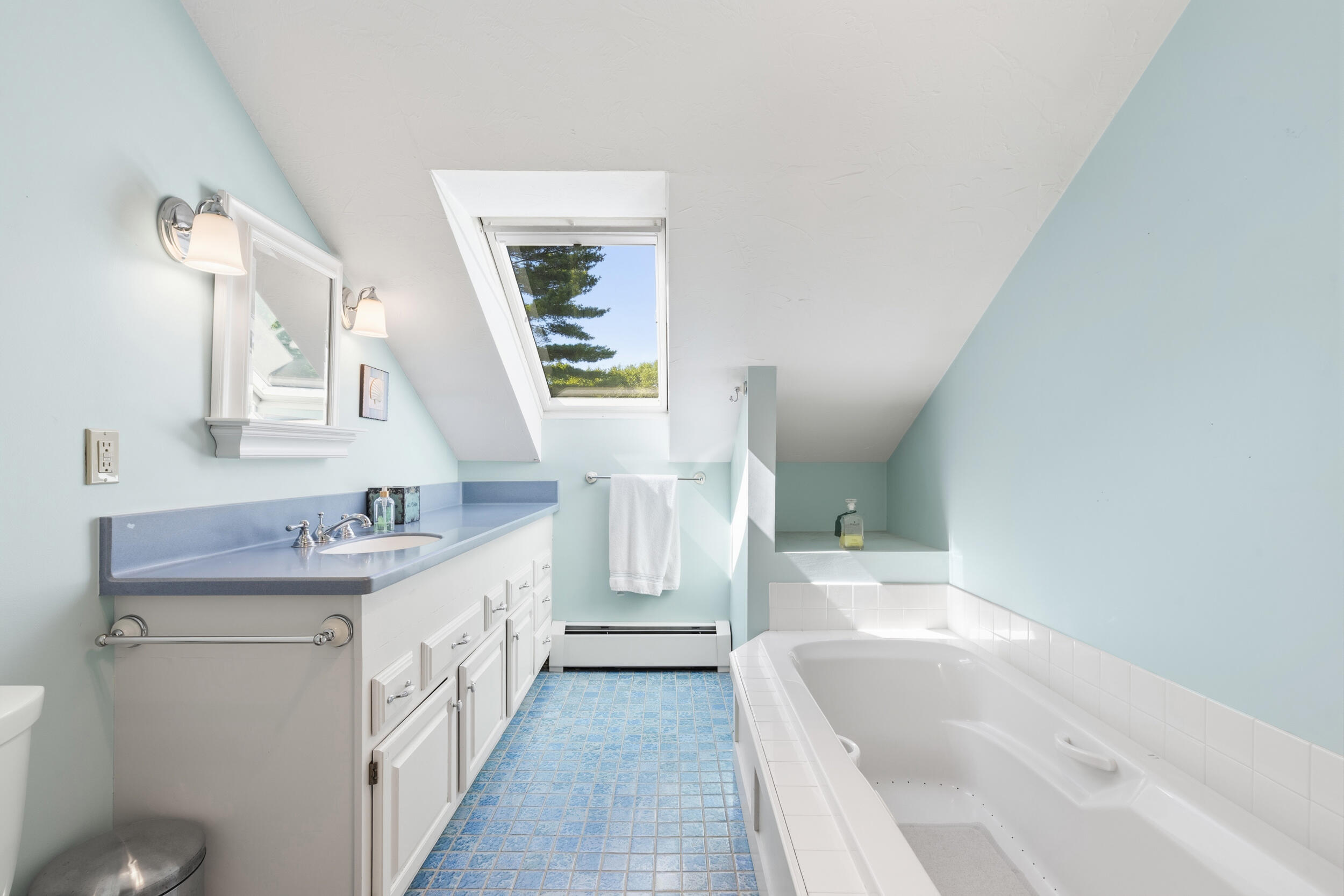 Bathroom with blue tile flooring, a built-in tub, and a skylight overlooking trees.