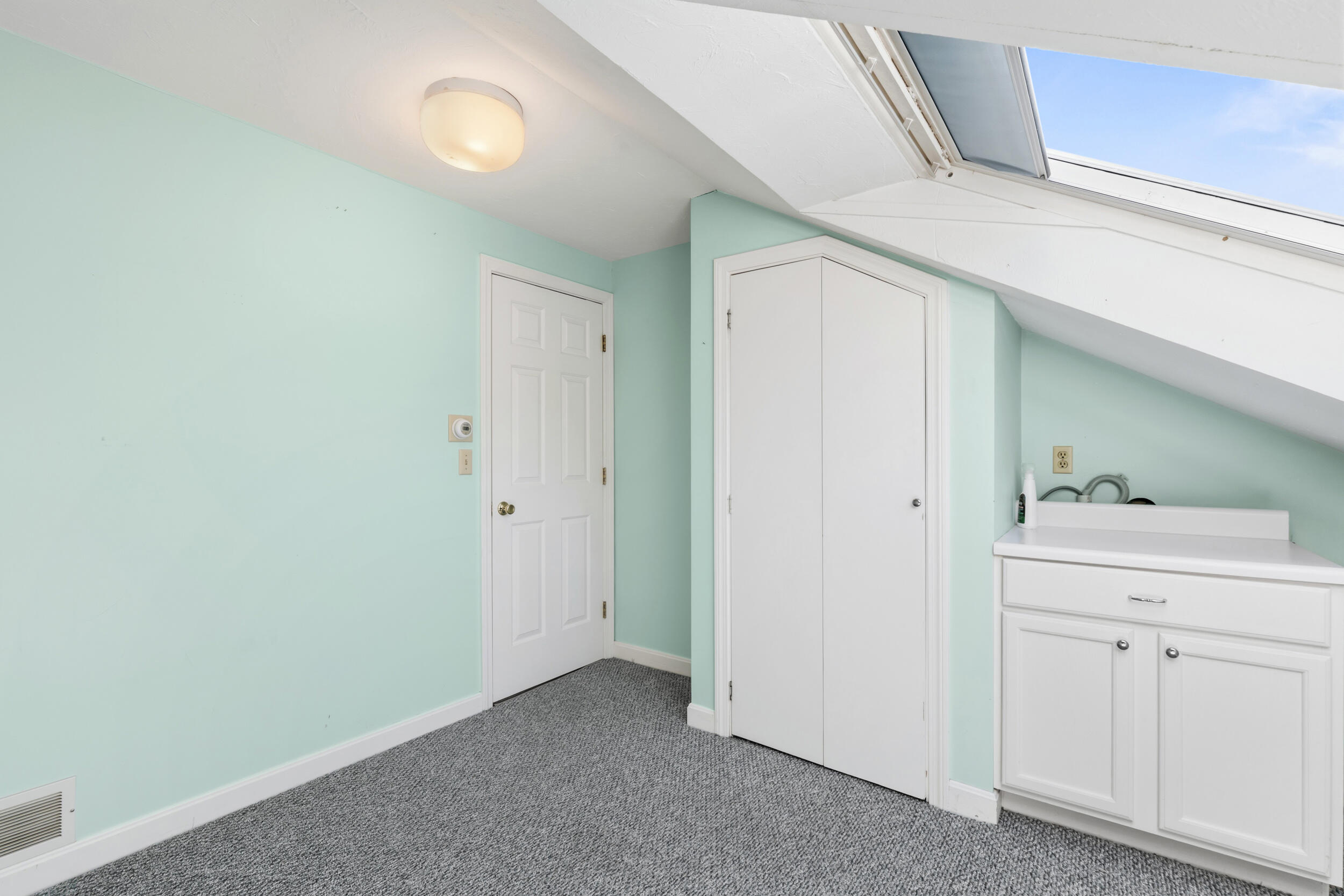 Attic bathroom with mint-green walls, a white vanity, gray carpet, and a skylight.