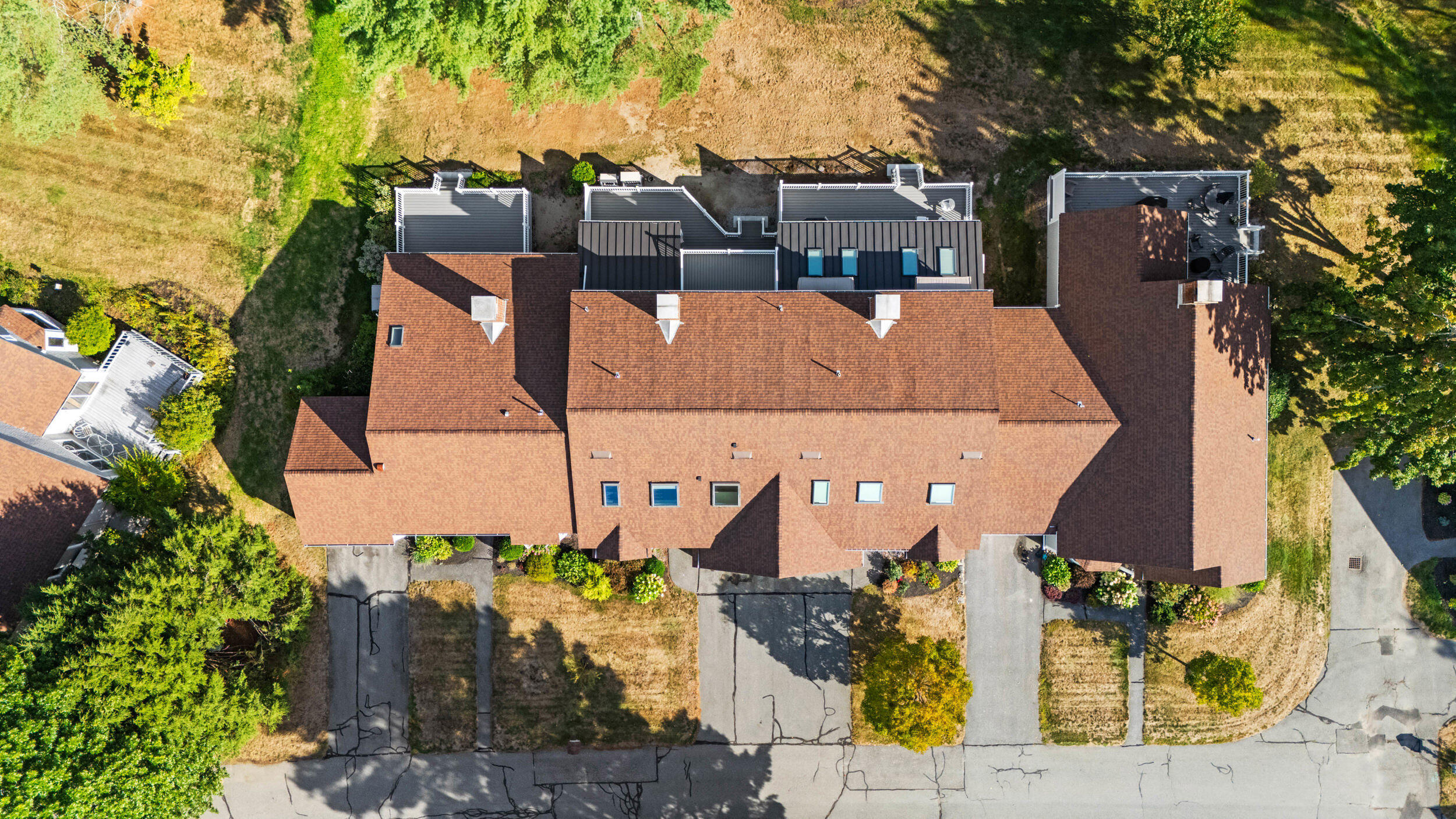 Aerial view of a residential building with connected roof sections, driveways, and surrounding trees.