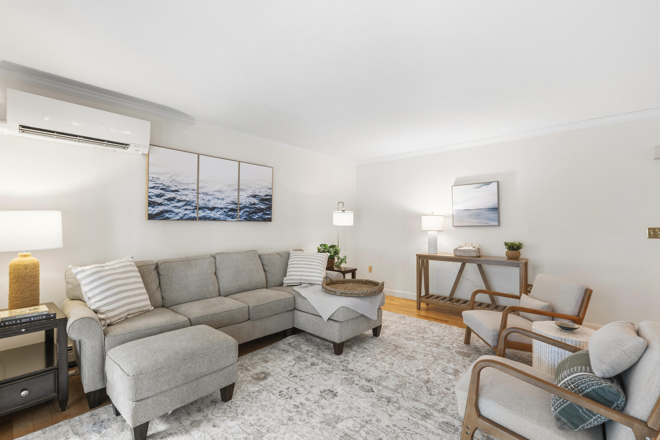Staged living room with a gray sectional, two armchairs, patterned rug, and ocean-themed artwork.