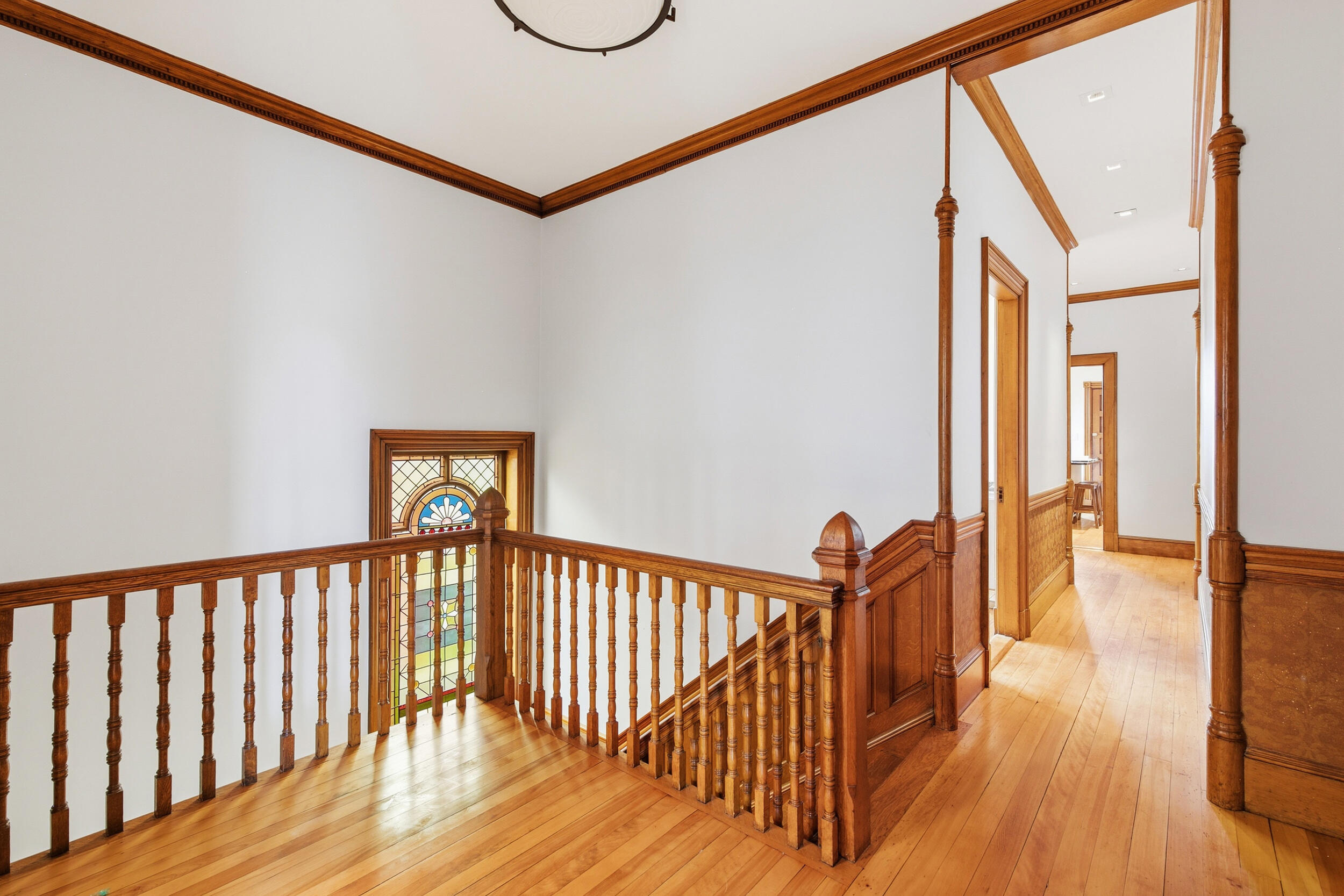 Wood-paneled stair landing with a stained-glass window, ornate railing, and polished hardwood floors.