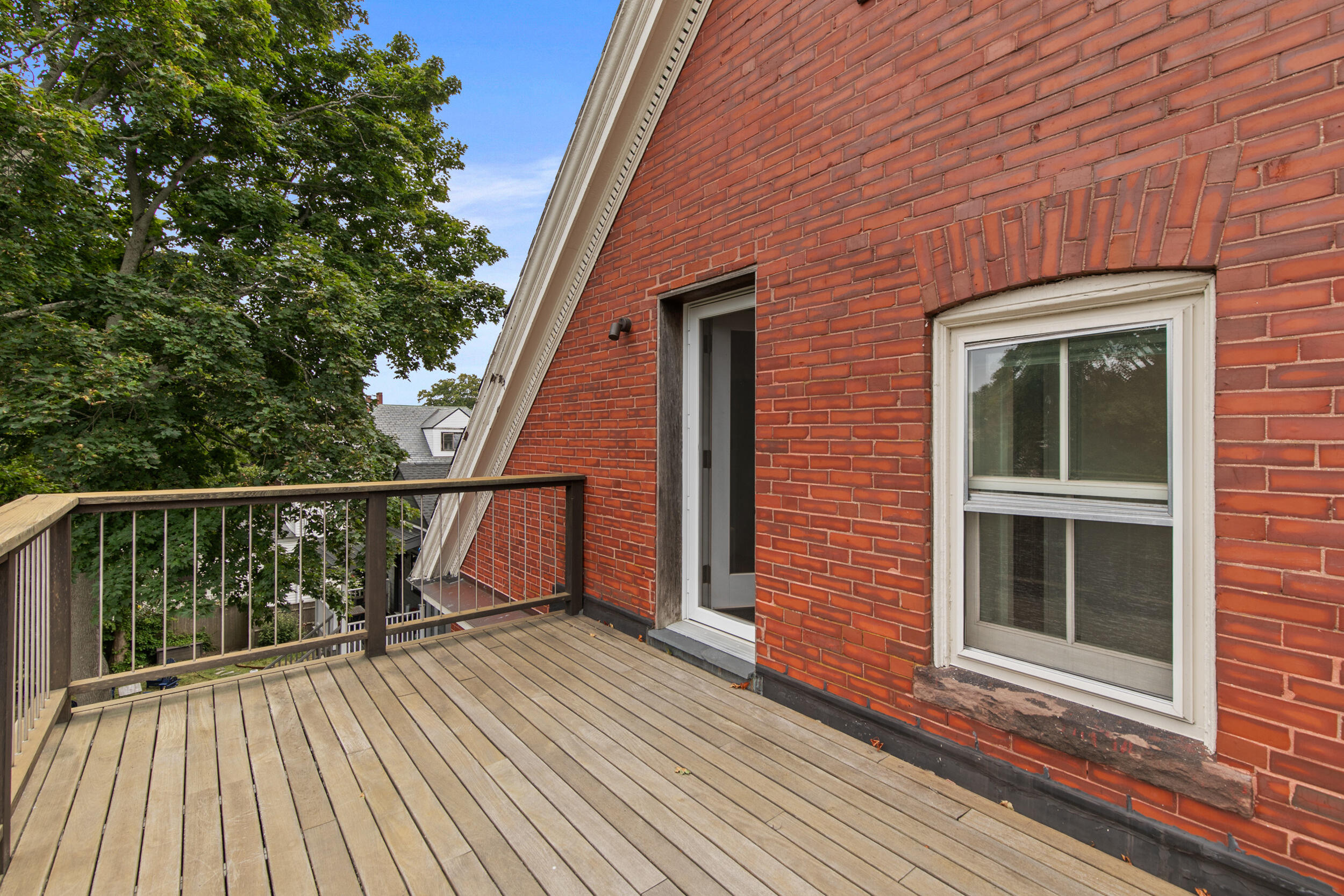 Wood-plank deck beside a red brick wall, with a glass door and white-trimmed window.