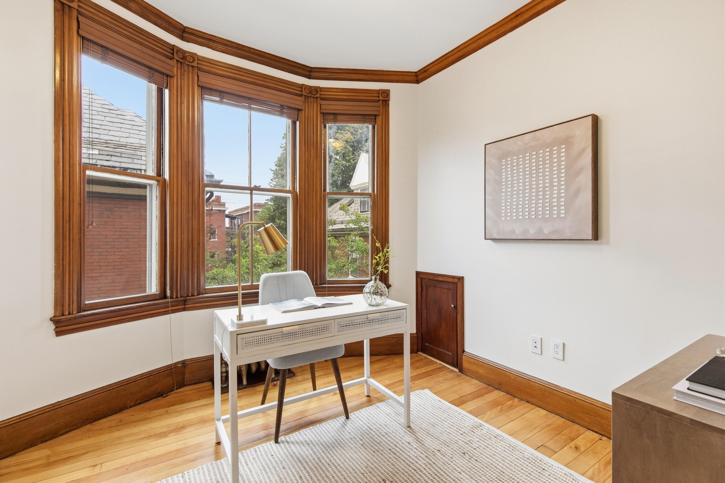 Staged study with a white desk beside tall, wood-trimmed windows.