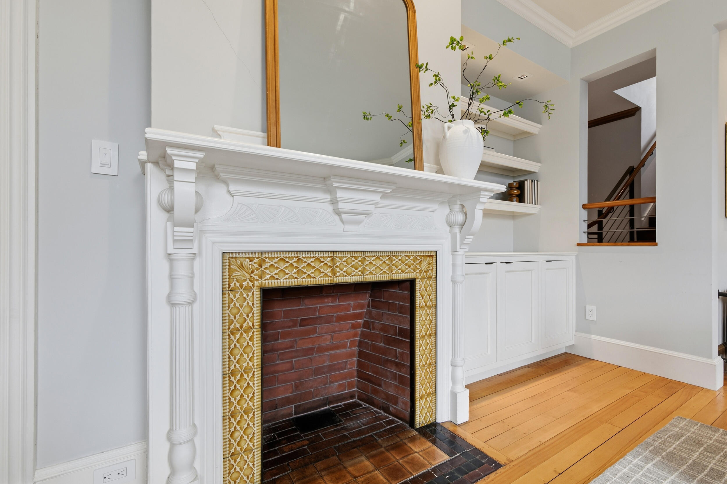 Living room fireplace with an ornate white mantel, patterned tile surround, and hardwood floors.