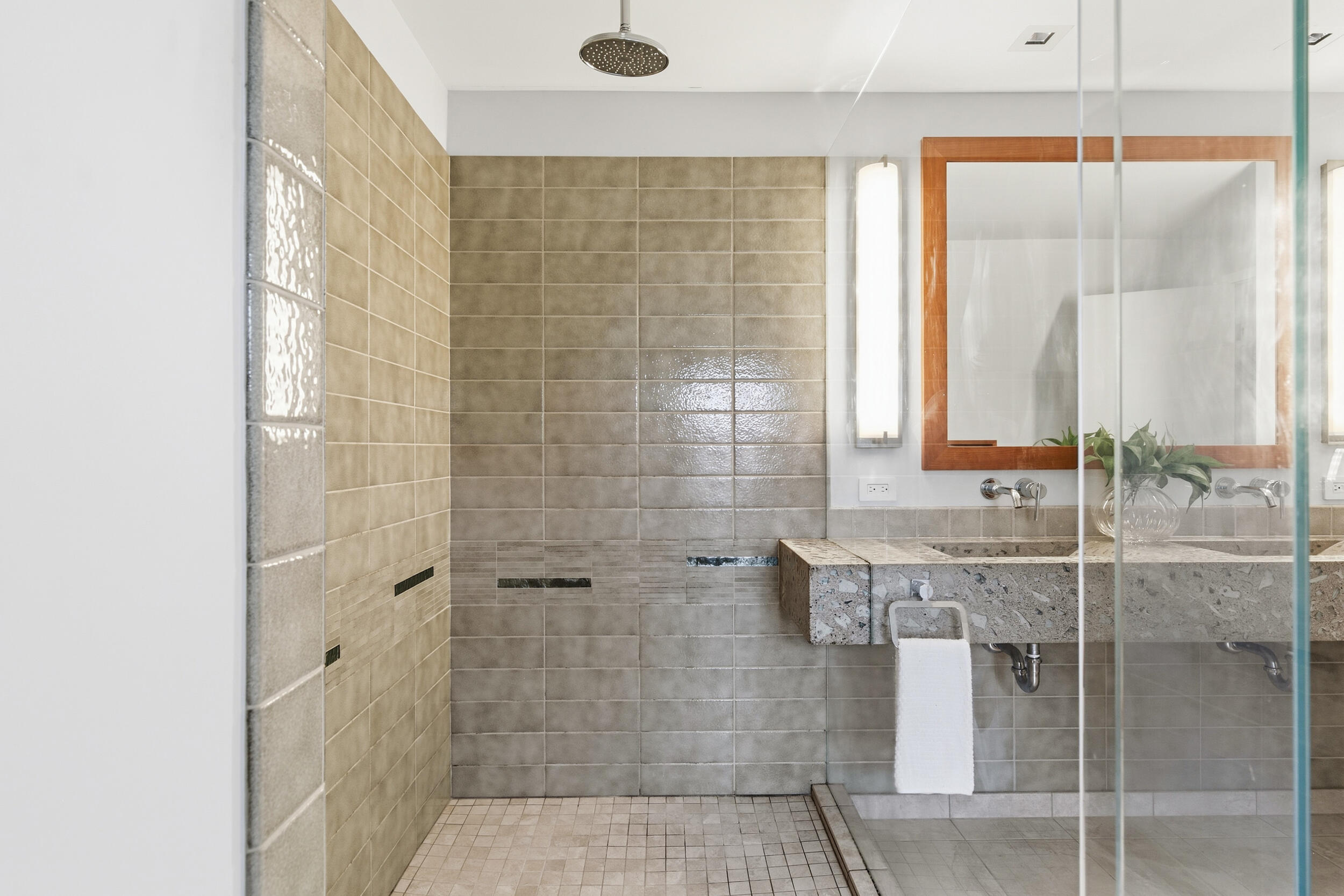 Tiled bathroom with a walk-in glass shower and a stone vanity beneath a wood-framed mirror.