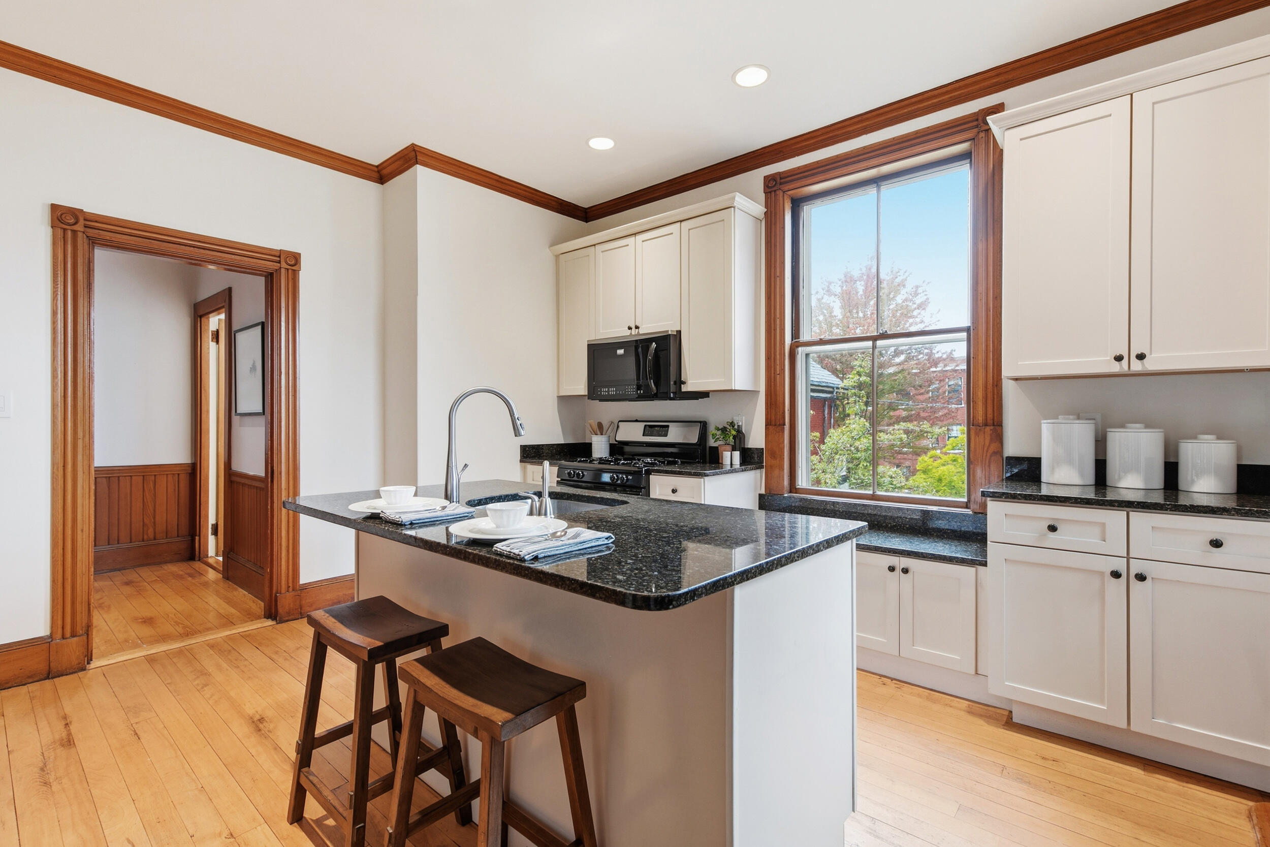 Kitchen with a black stone island, white cabinetry, and distinctive wood trim around the window and doorway.