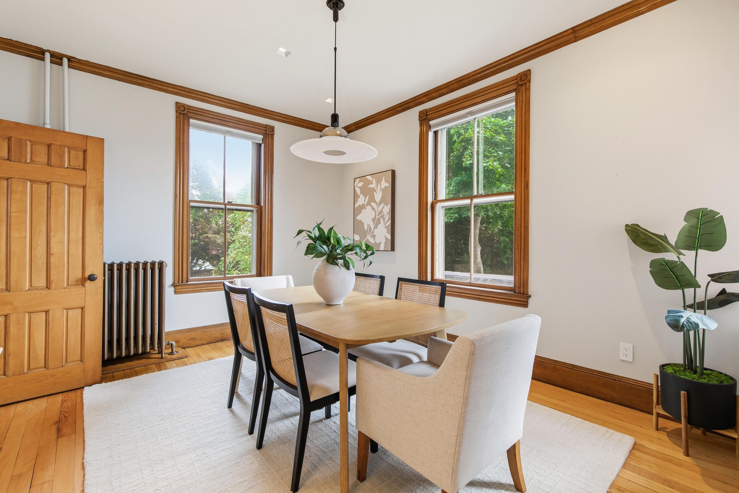 Dining room with a wood table, cane-back chairs, and tall windows framed in rich wood trim.