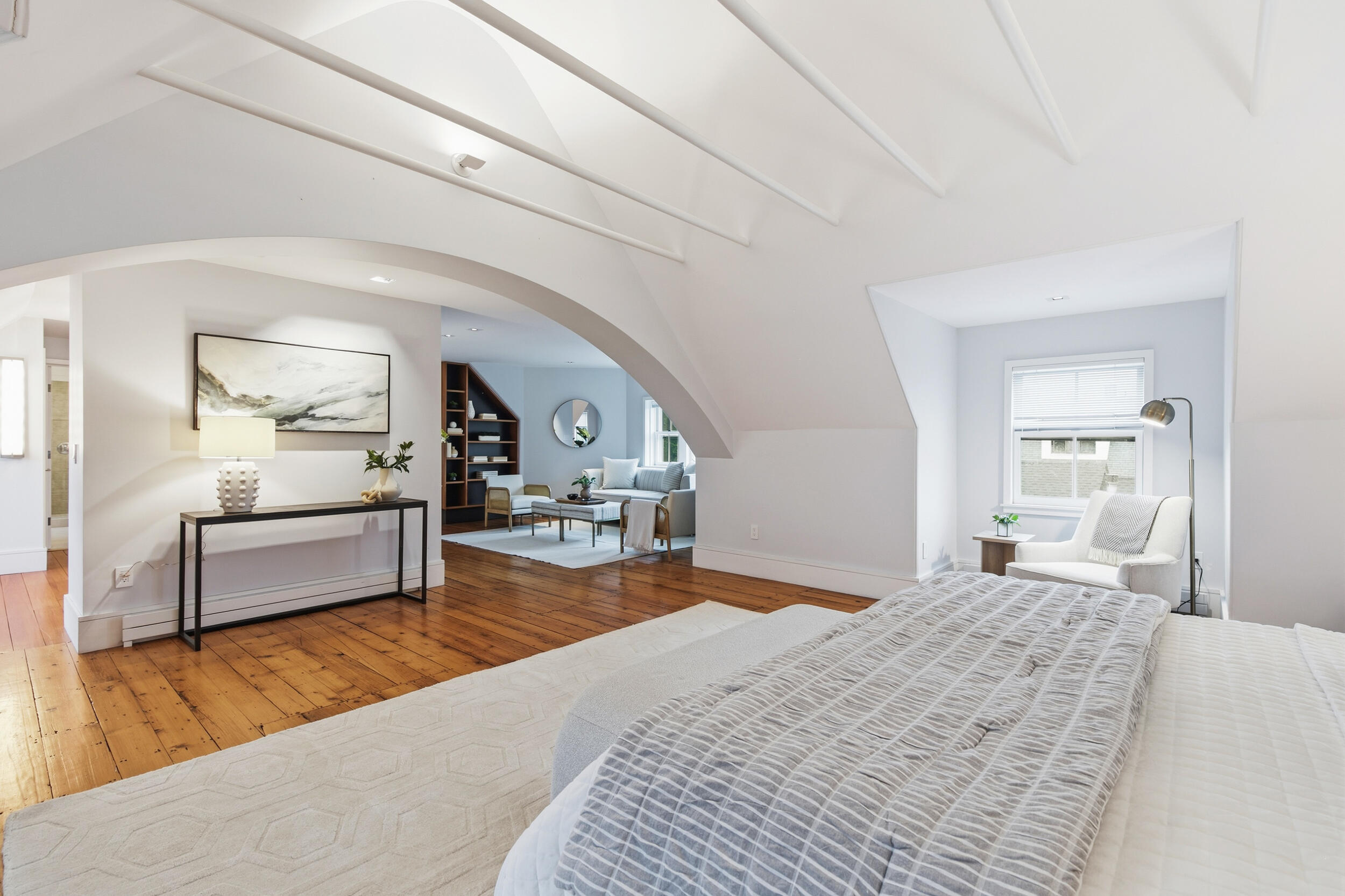 Bright bedroom with exposed ceiling beams, a large bed, and an arched opening to a sitting area.
