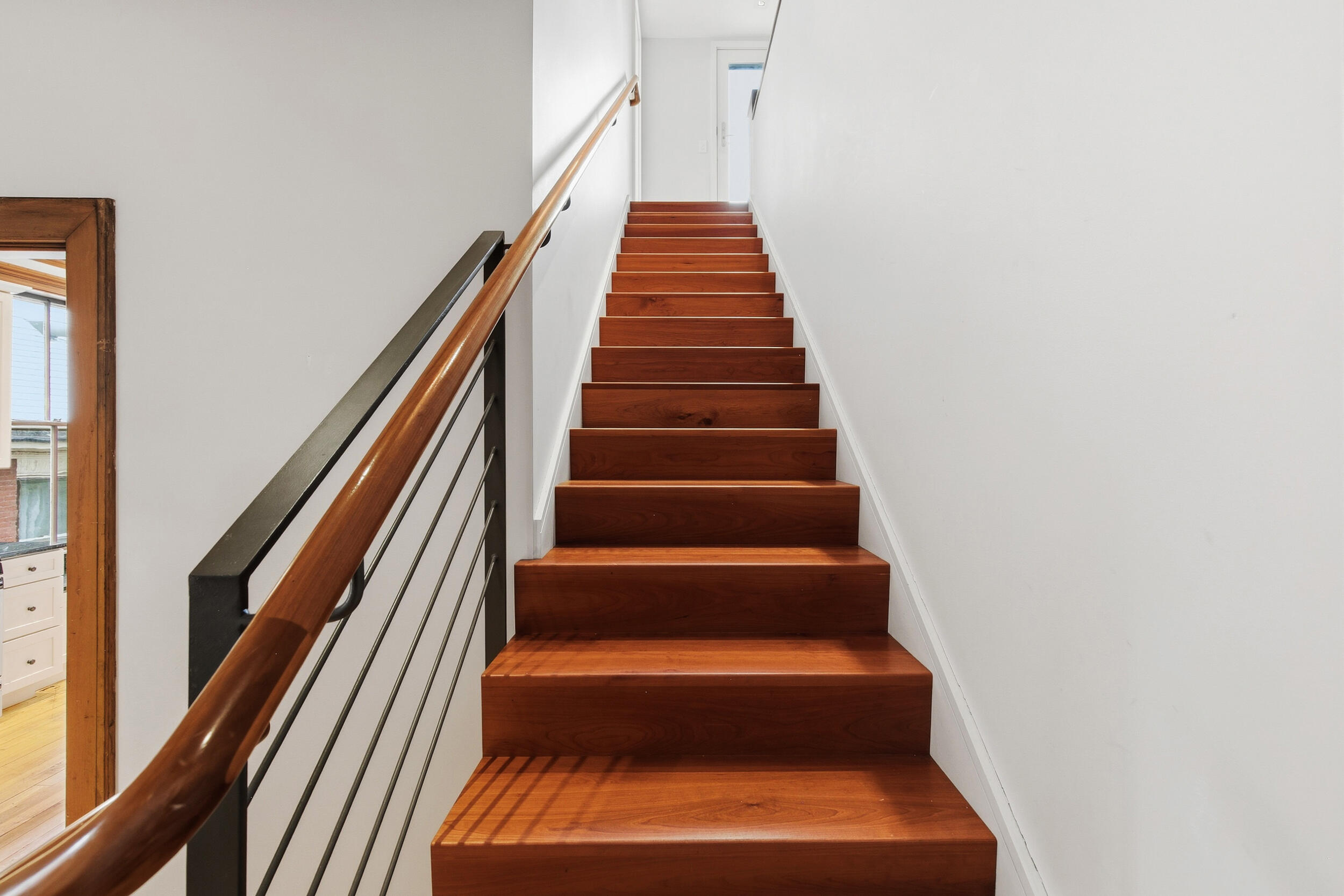 Wooden staircase with a polished handrail and black metal railing.