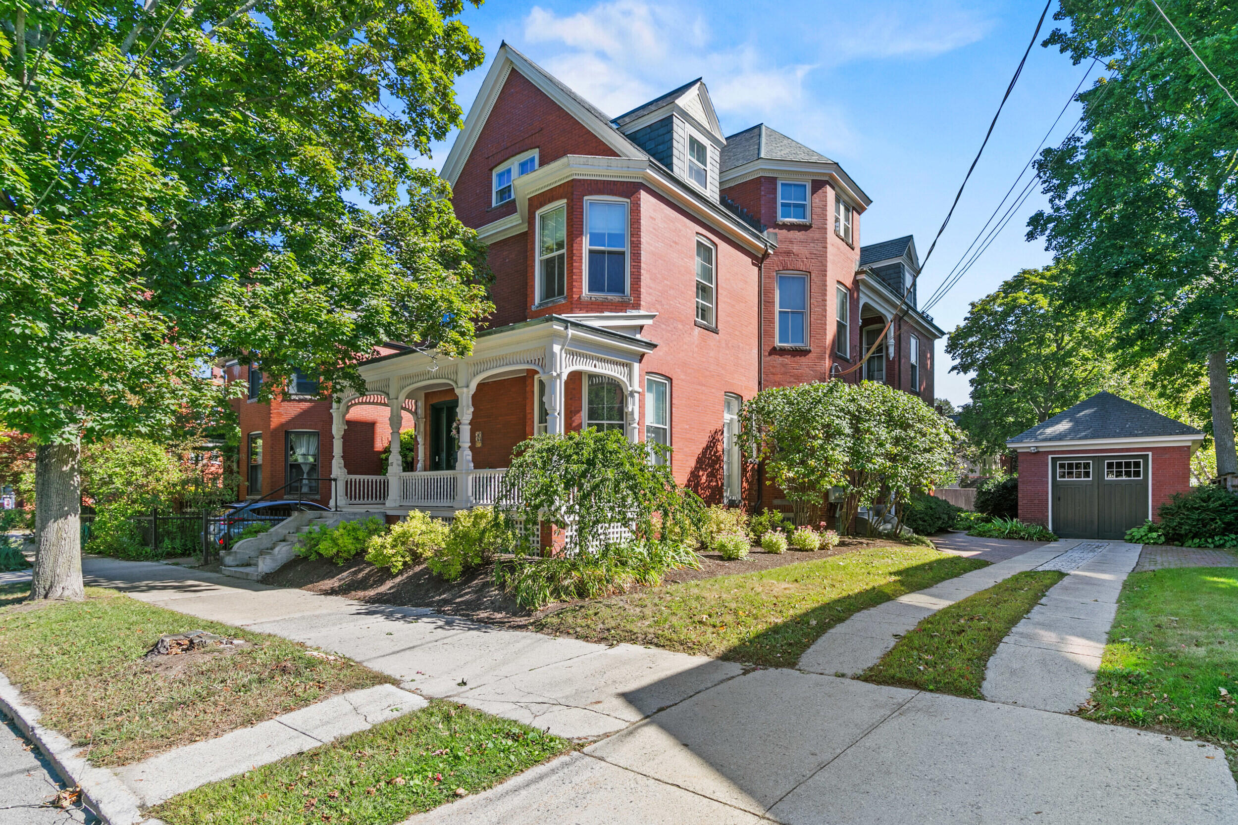 Multi-story red brick house with an ornate white porch and detached garage