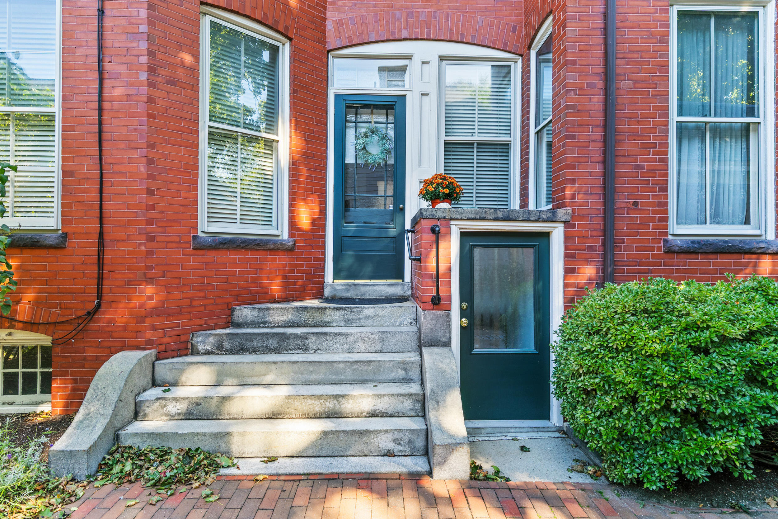 Brick building entrance with two dark teal doors and broad stone steps.