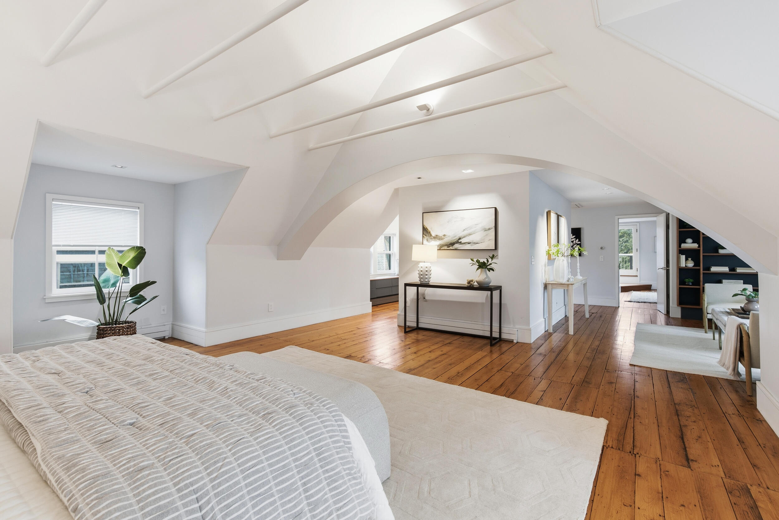 Staged attic bedroom with a vaulted beam ceiling, hardwood floors, and a bed beneath a window.