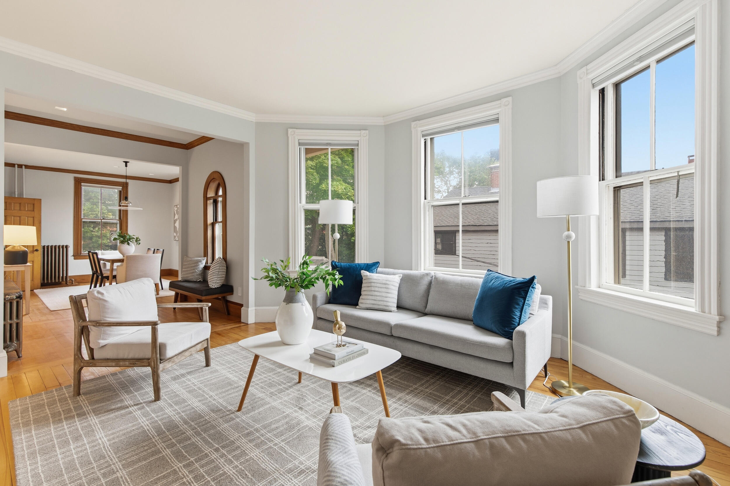 Staged living room with large windows, hardwood floors, and an adjoining dining area.