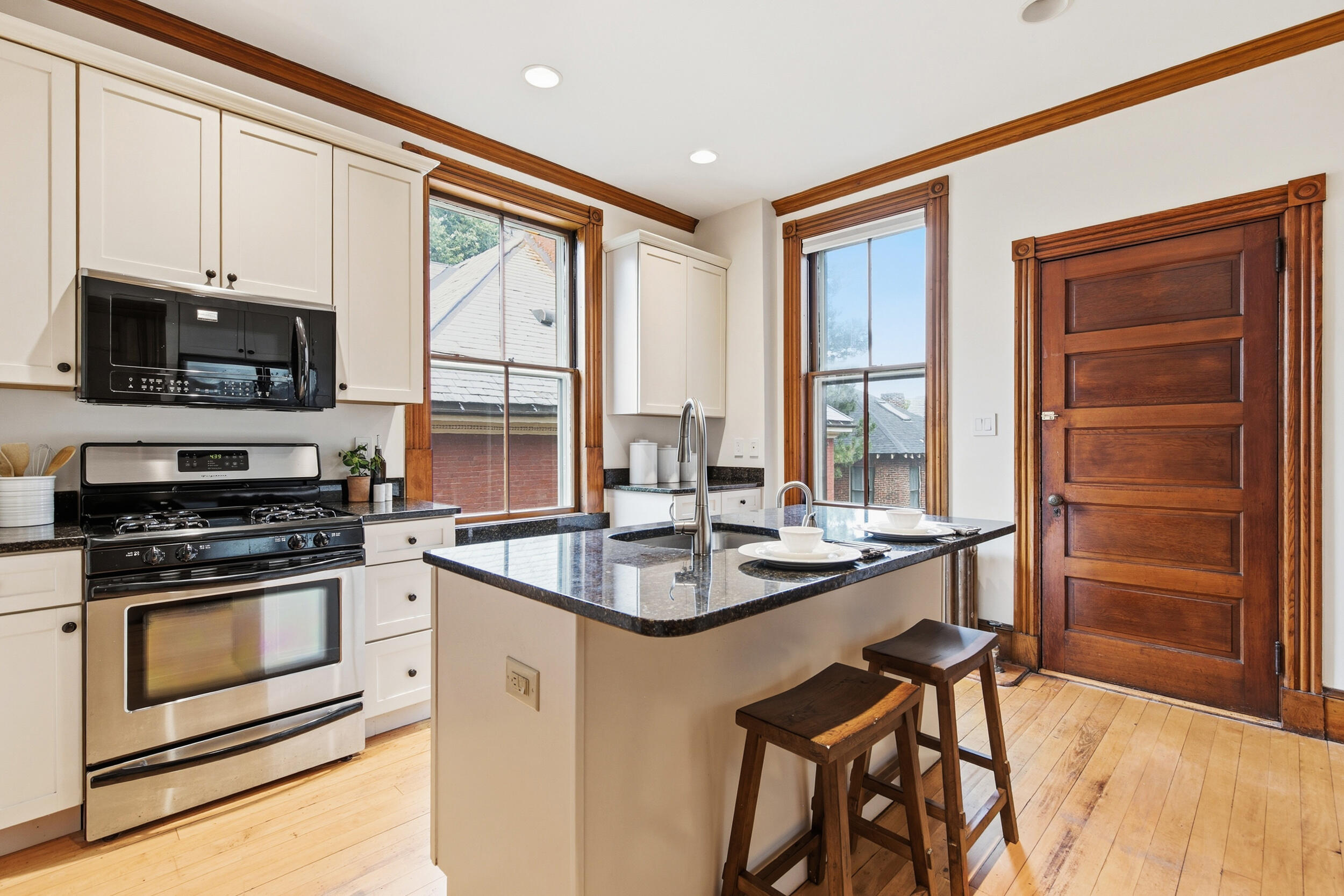 Kitchen with a granite island, white cabinetry, stainless appliances, and wood-trimmed windows and door.