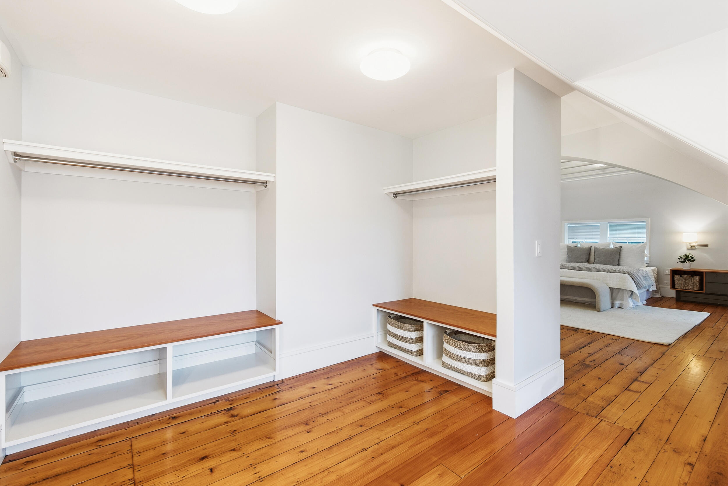 Walk-in closet with built-in shelves and hanging rods beside a bedroom with hardwood floors.