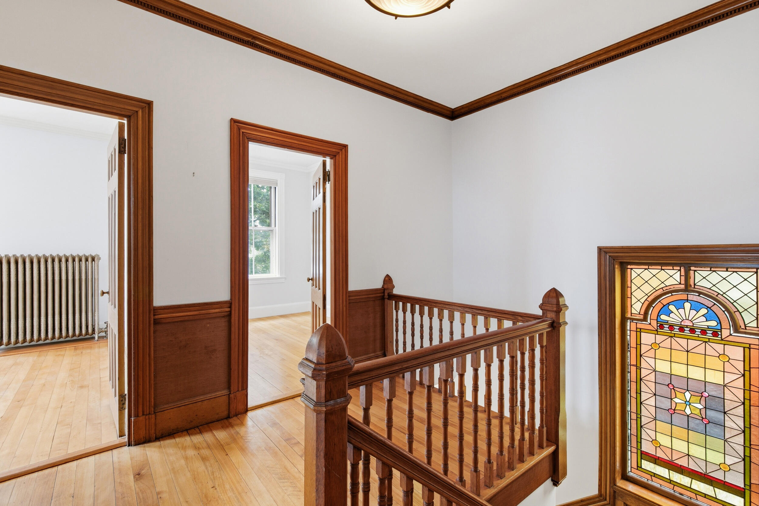 Interior stair landing with a wooden balustrade, hardwood floors, and a stained-glass window.
