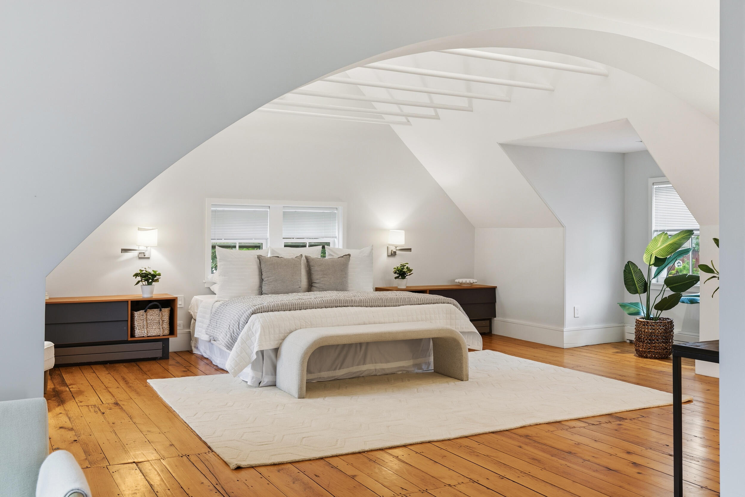 Staged attic bedroom with a white bed, sloped ceiling, and warm wood floors.