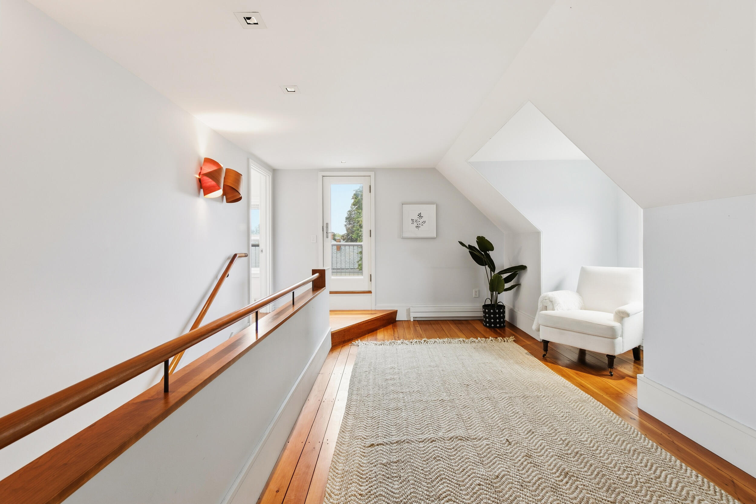 Bright attic sitting area with a white armchair, wood floors, and a glass door to a balcony.