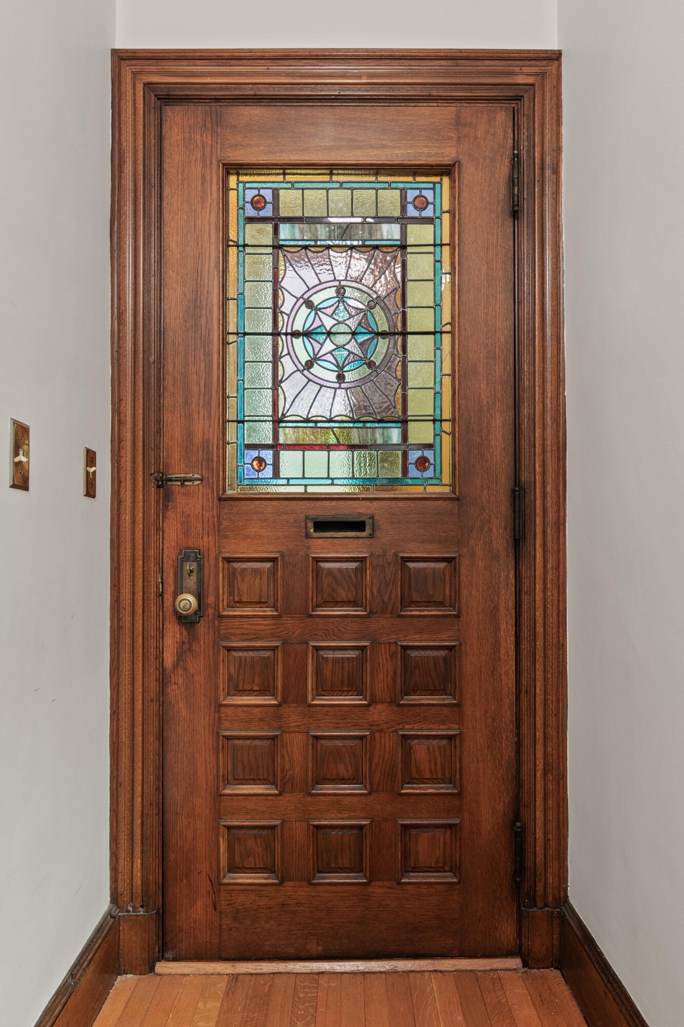 Wooden entry door with colorful stained-glass panel and raised panels.