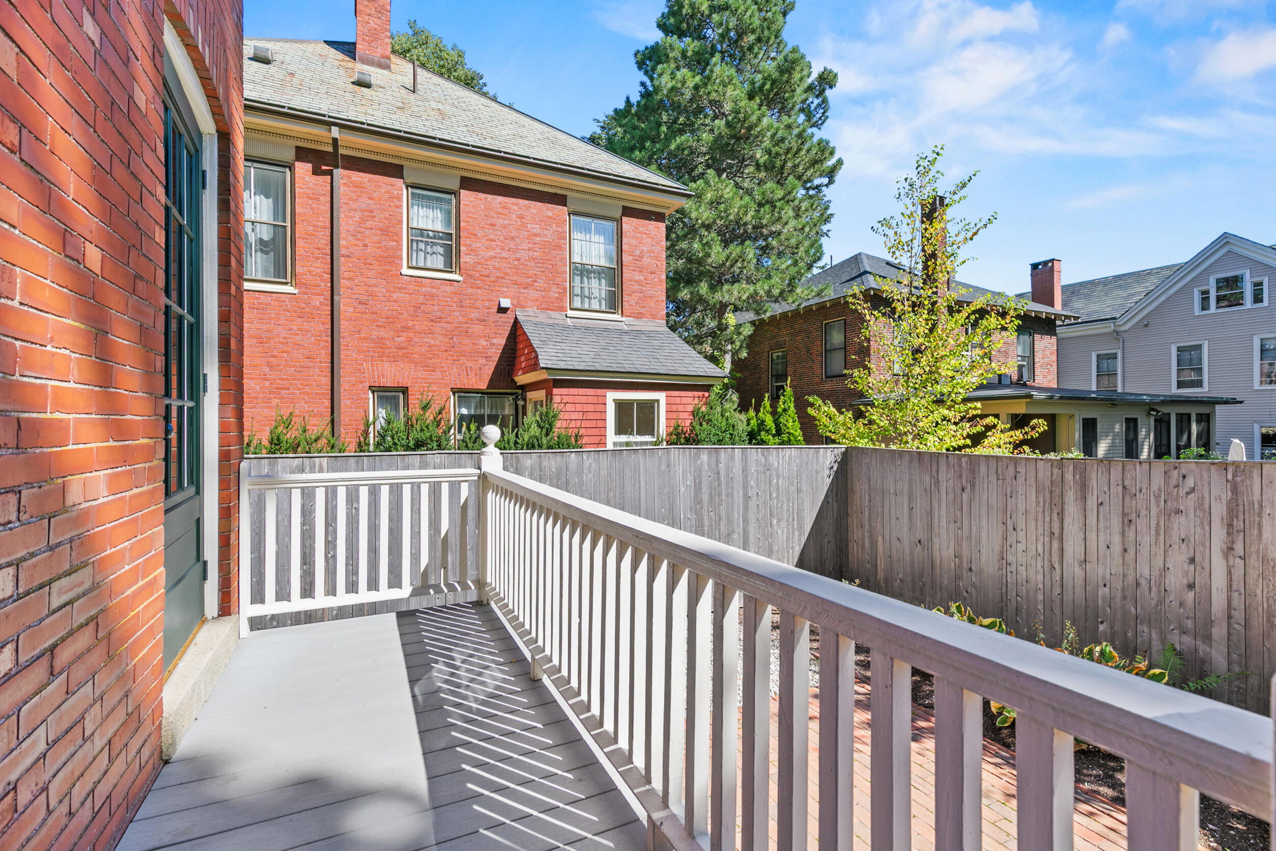 Brick home's raised deck with white railing overlooking a fenced yard and neighboring houses.