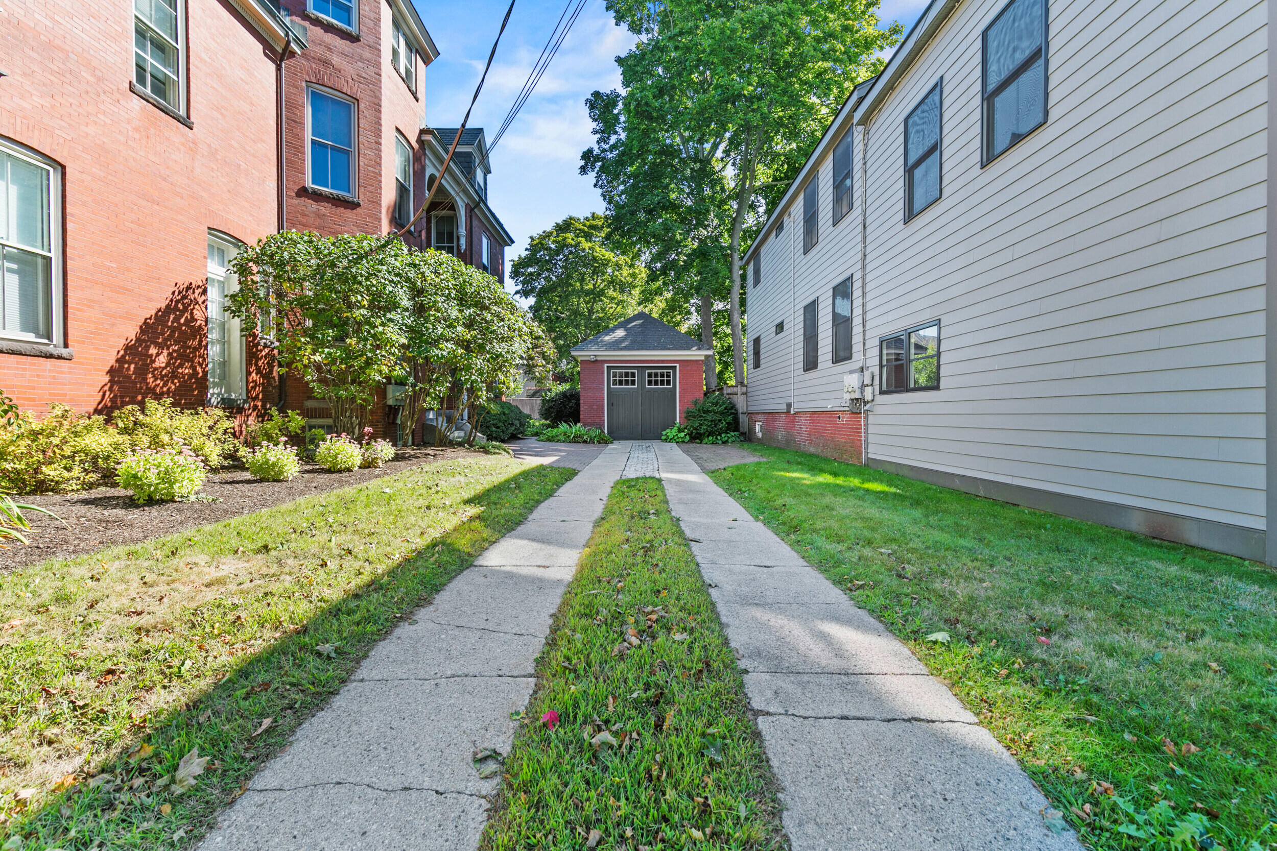 Driveway between brick and clapboard buildings leading to a detached garage.