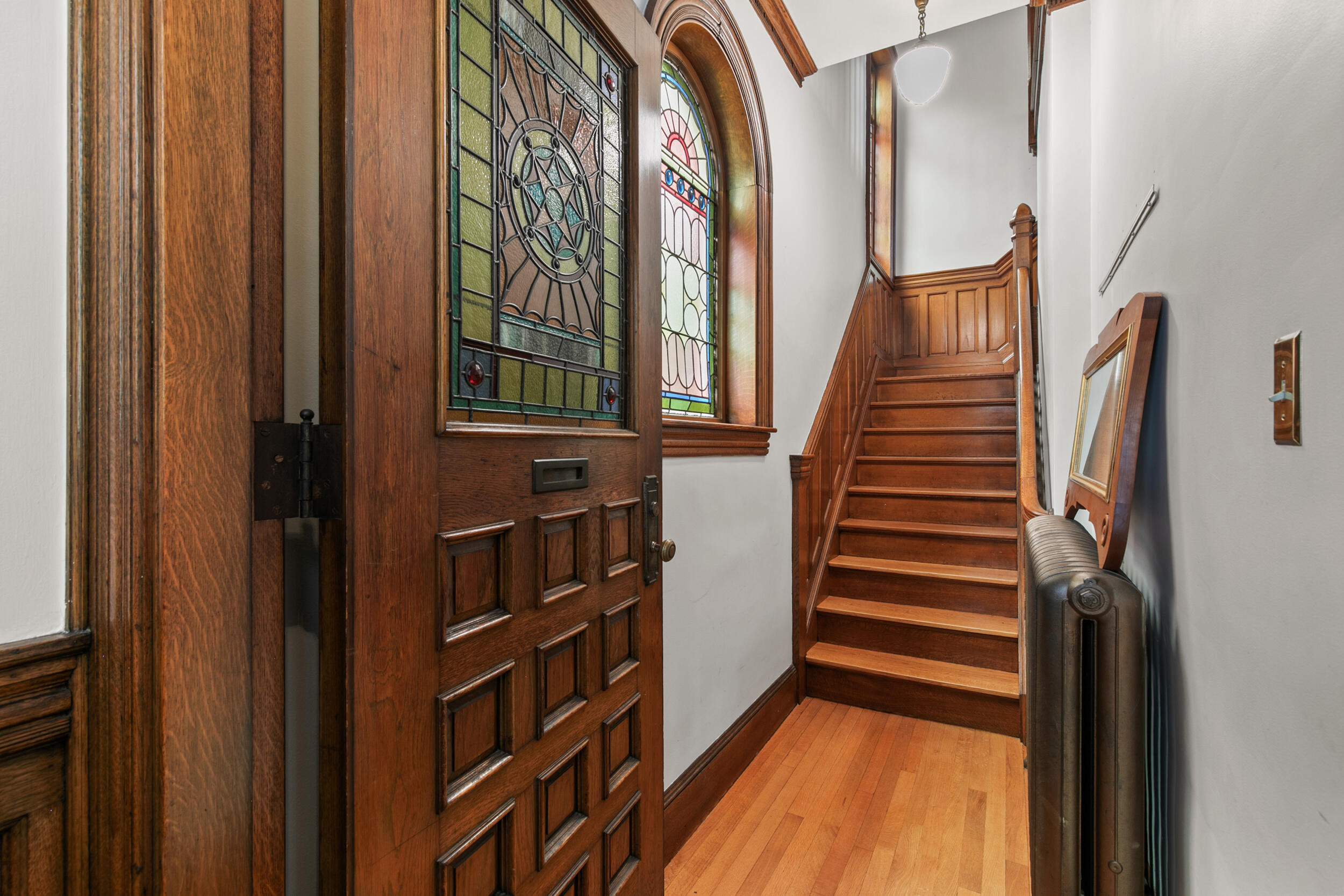 Entry hall with an ornate stained-glass door, arched window, and polished wood staircase.