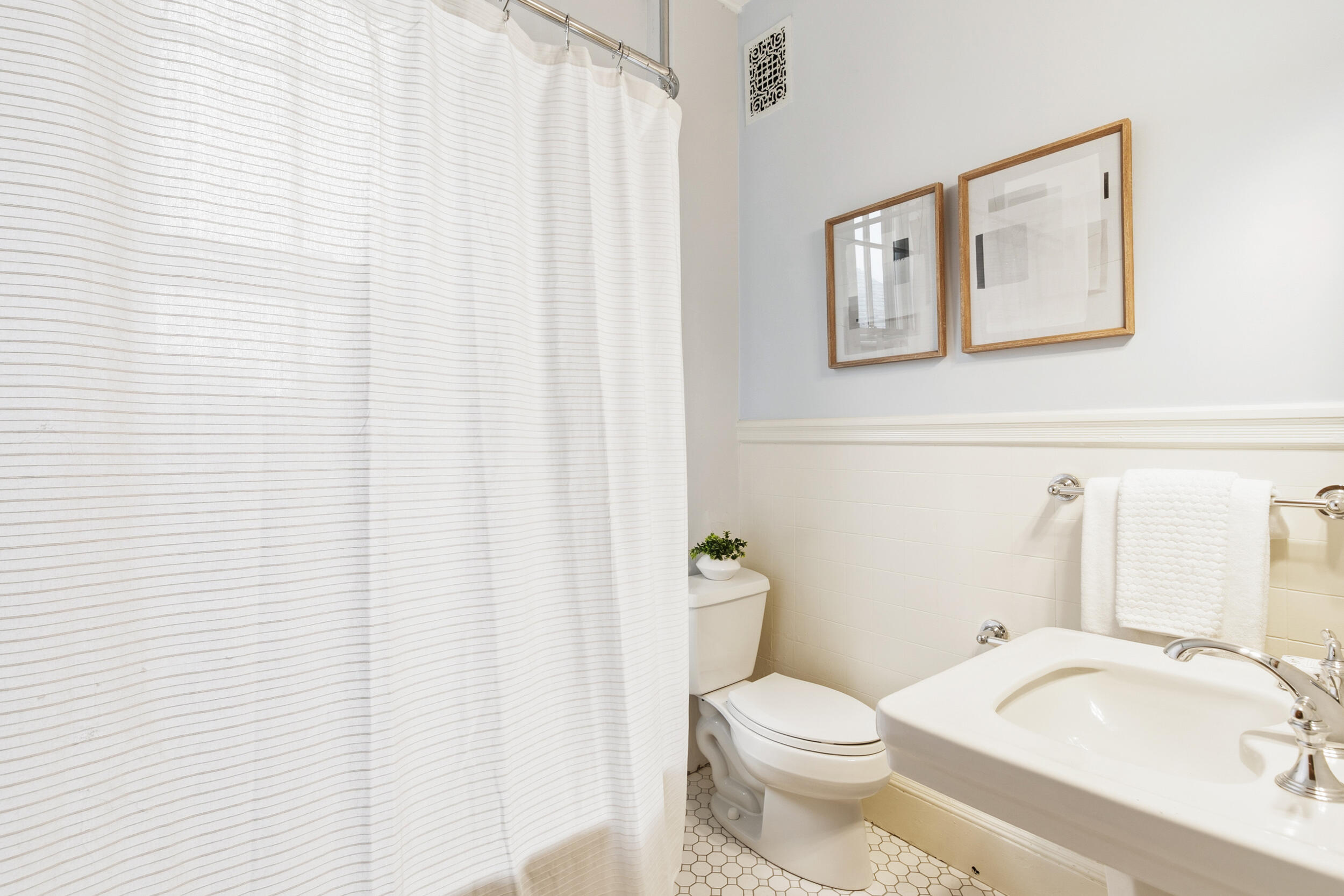 Bathroom with a striped shower curtain, hexagonal tile floor, and pedestal sink.