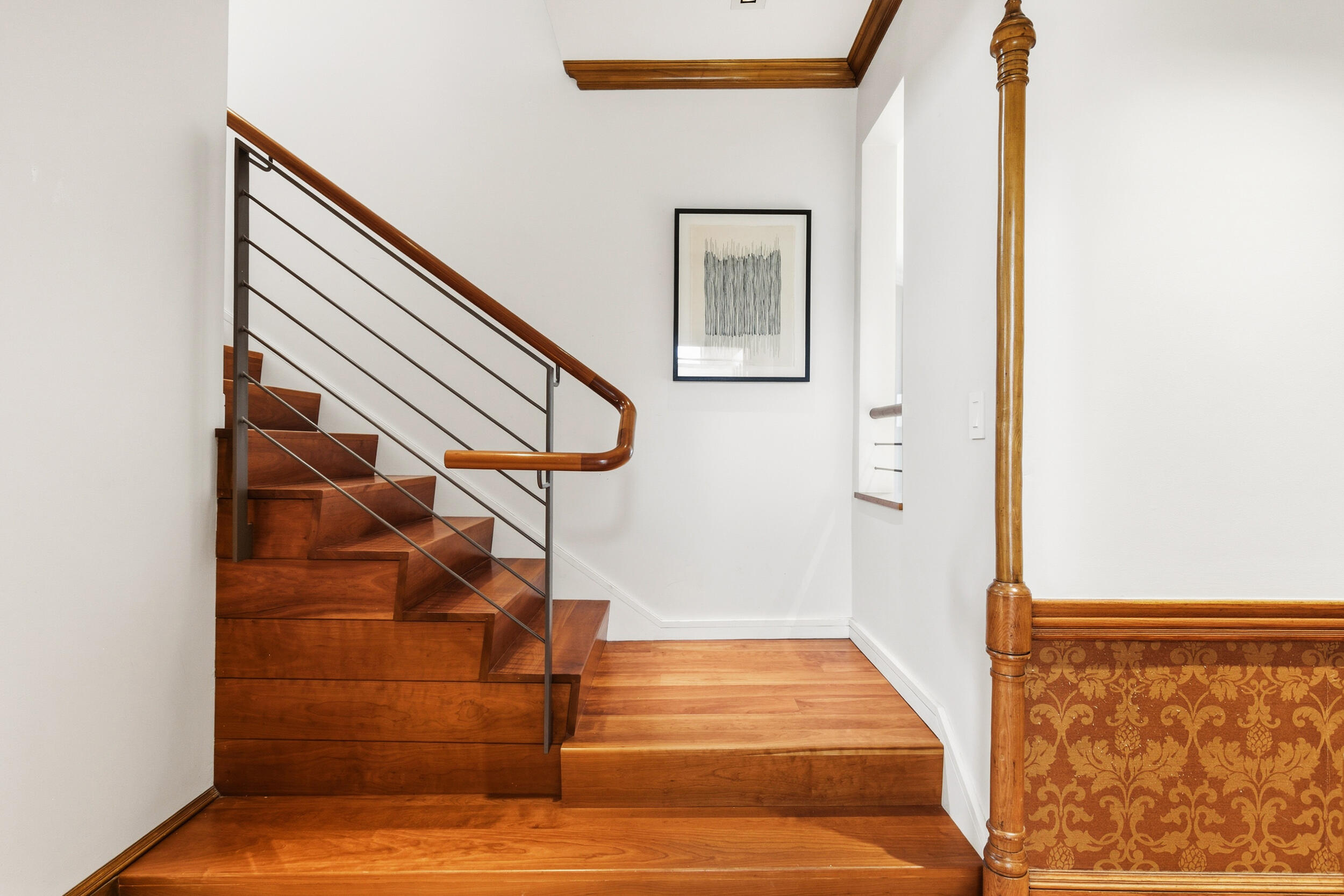Wooden staircase with metal railings, patterned wall paneling, and framed artwork.