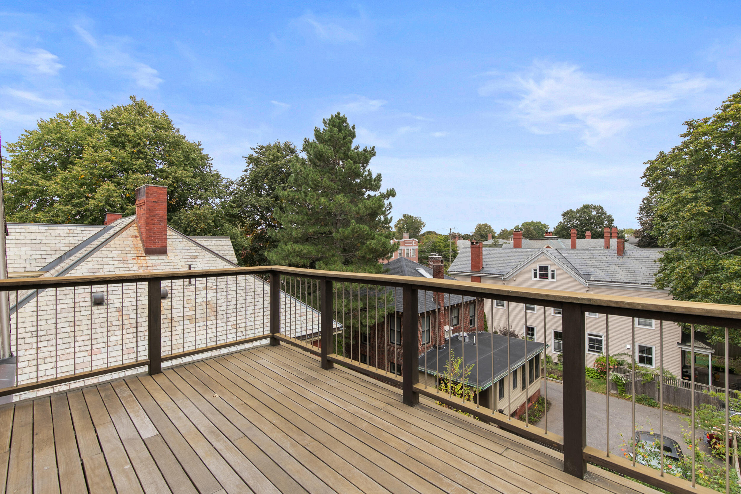Elevated wooden deck with dark railings overlooking neighboring homes and leafy trees.