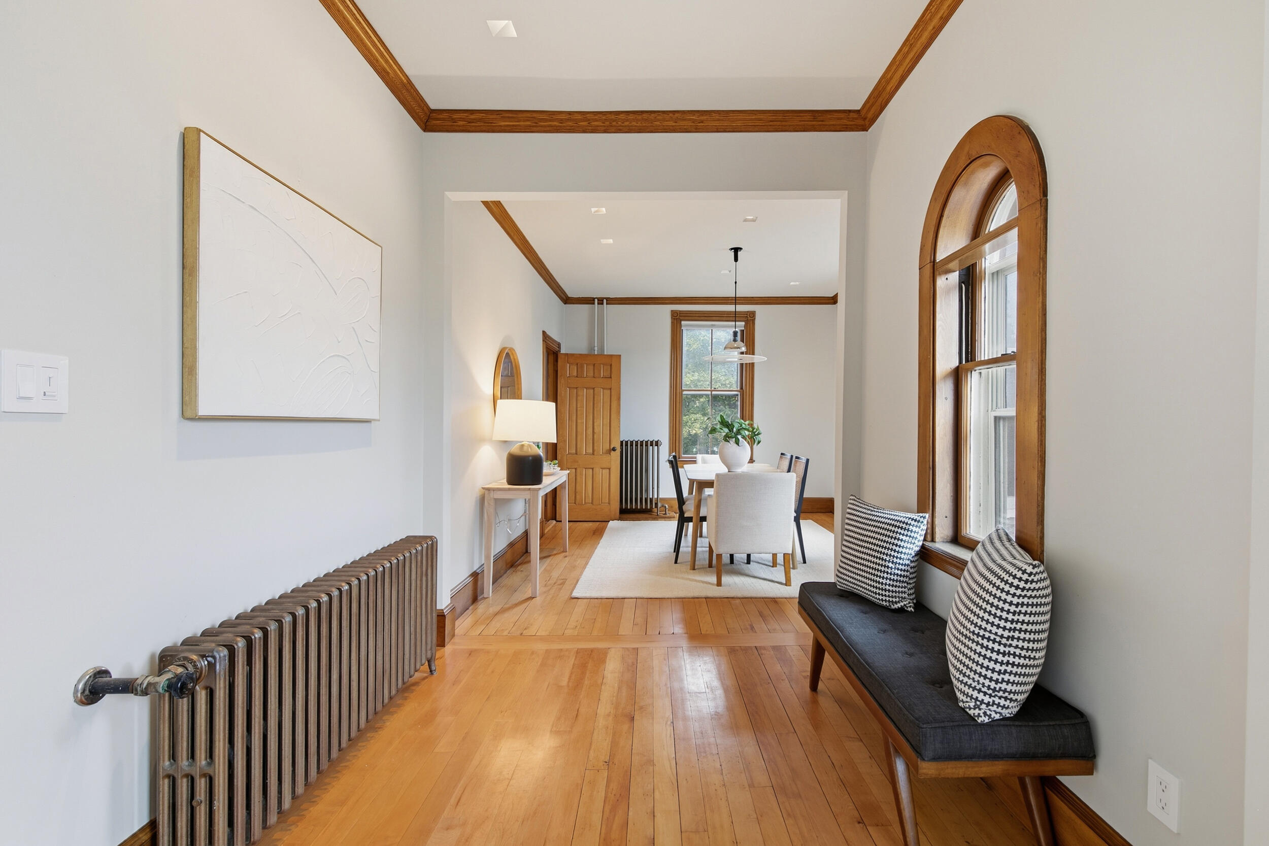 Dining area with hardwood floors, wood-trimmed arched windows, and a table set near a window seat.