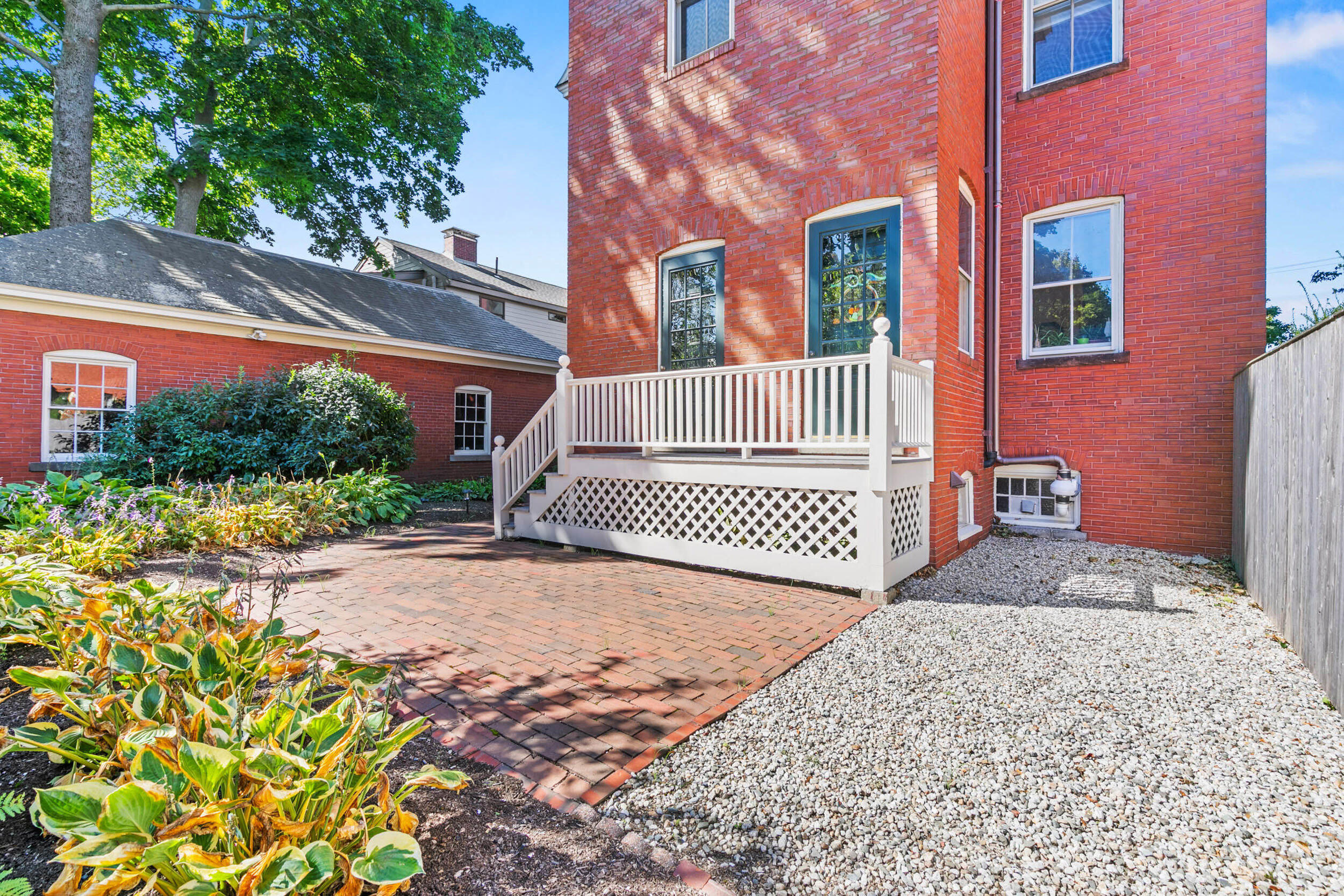 Red brick home with a white-railed deck beside a brick patio and landscaped garden.