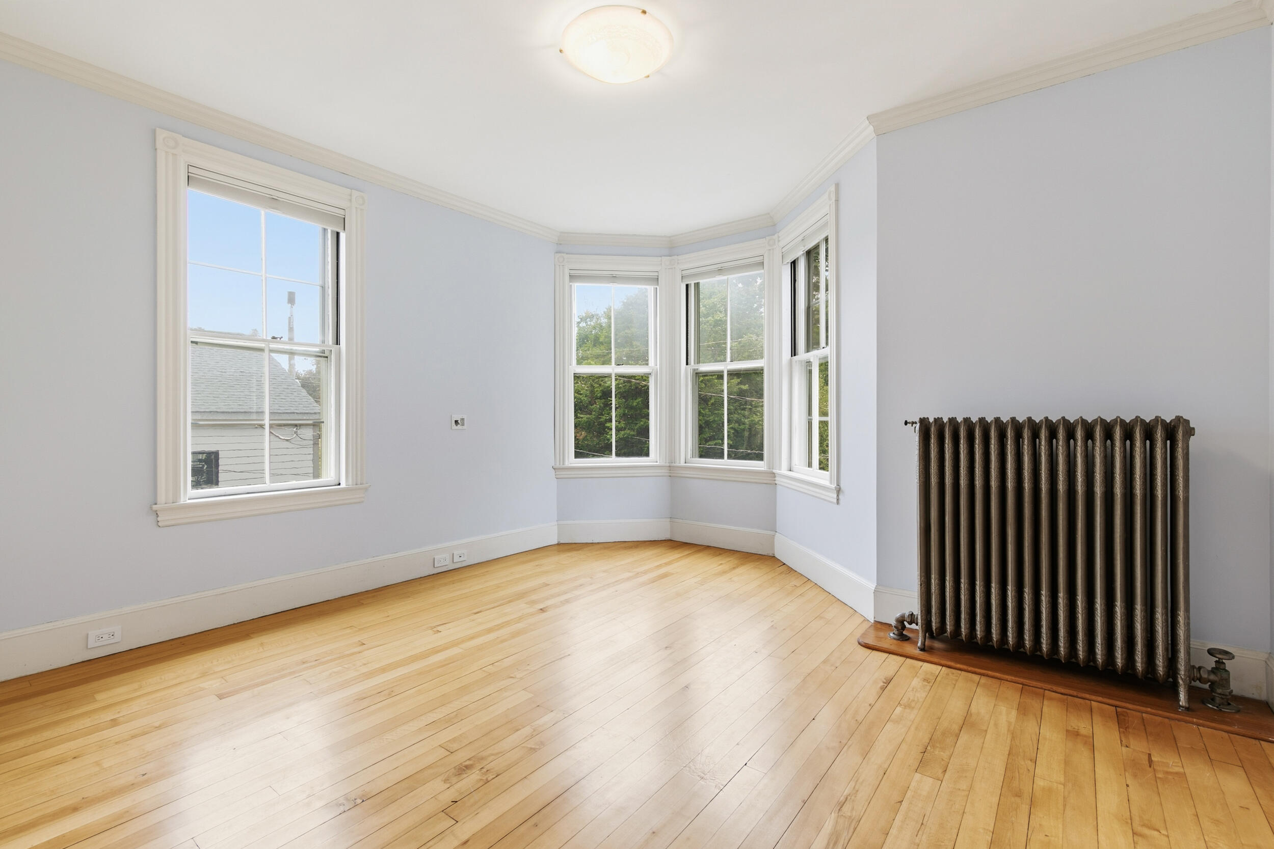 Empty room with hardwood floors, a bay window, and a cast-iron radiator.