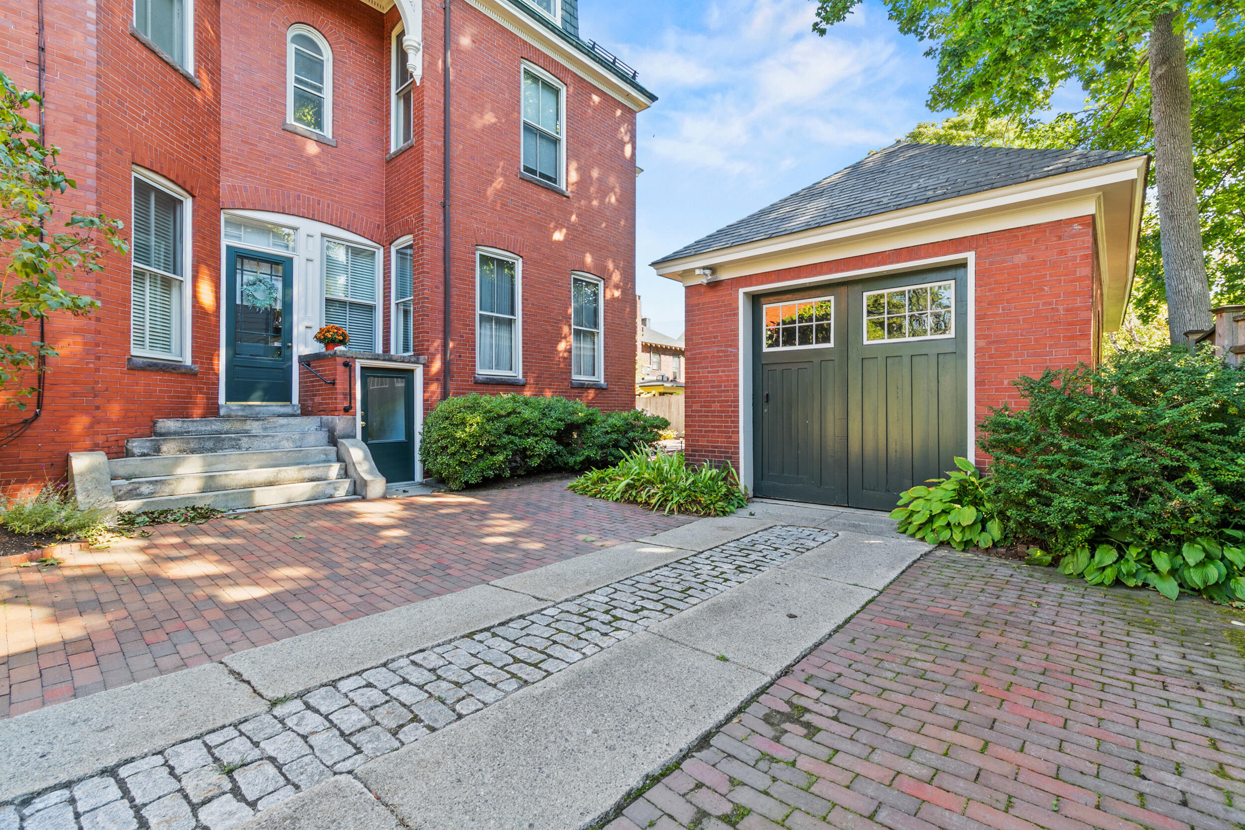 Red-brick home and detached garage with dark green doors, brick courtyard, and stone walkway.