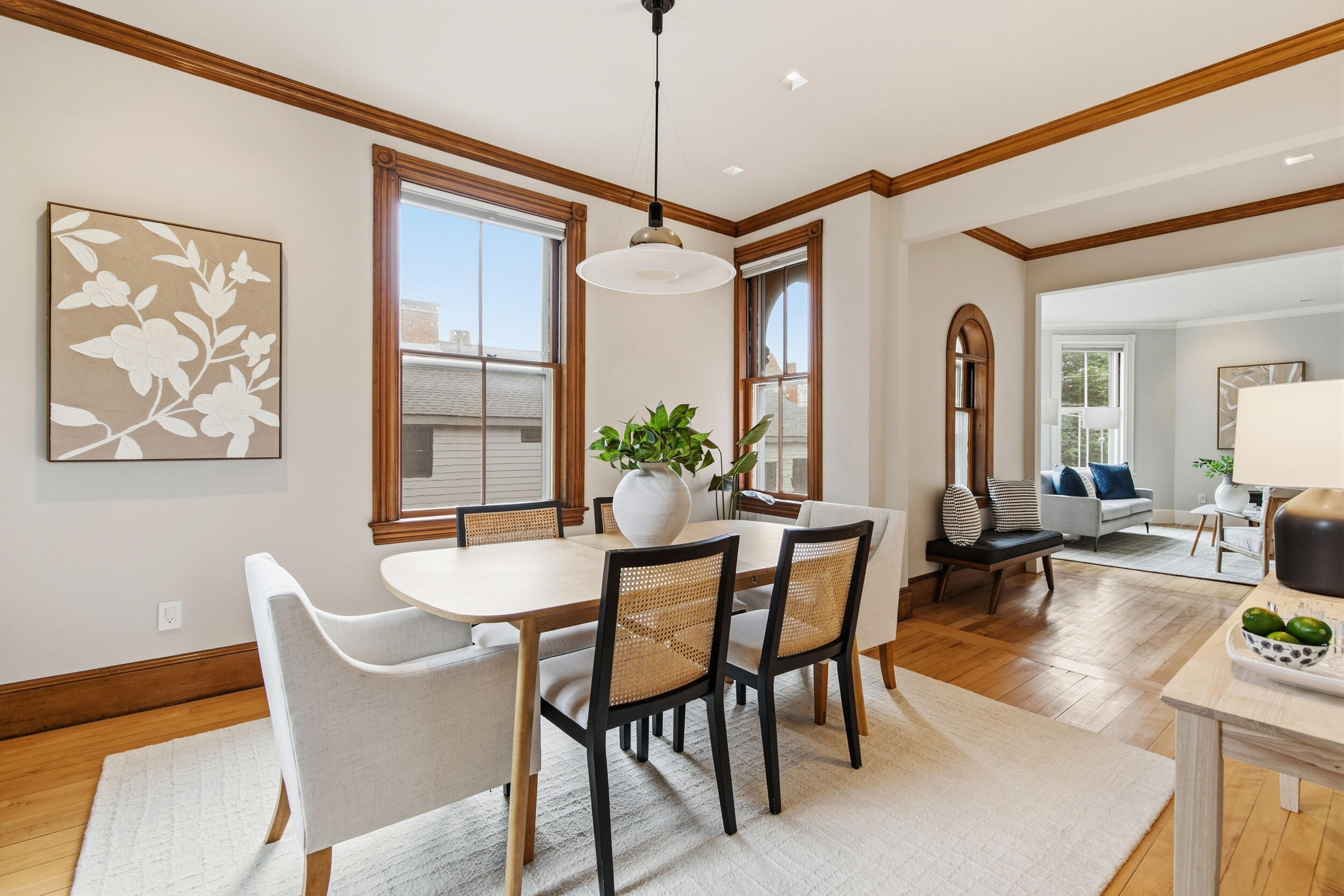 Dining room with a set table, tall wood-trimmed windows, and an adjoining living room.