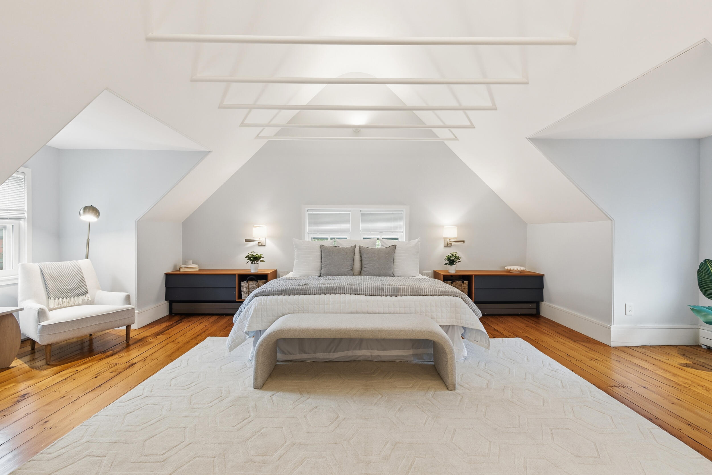 Staged attic bedroom with a centered bed, warm wood floors, and a white geometric ceiling.
