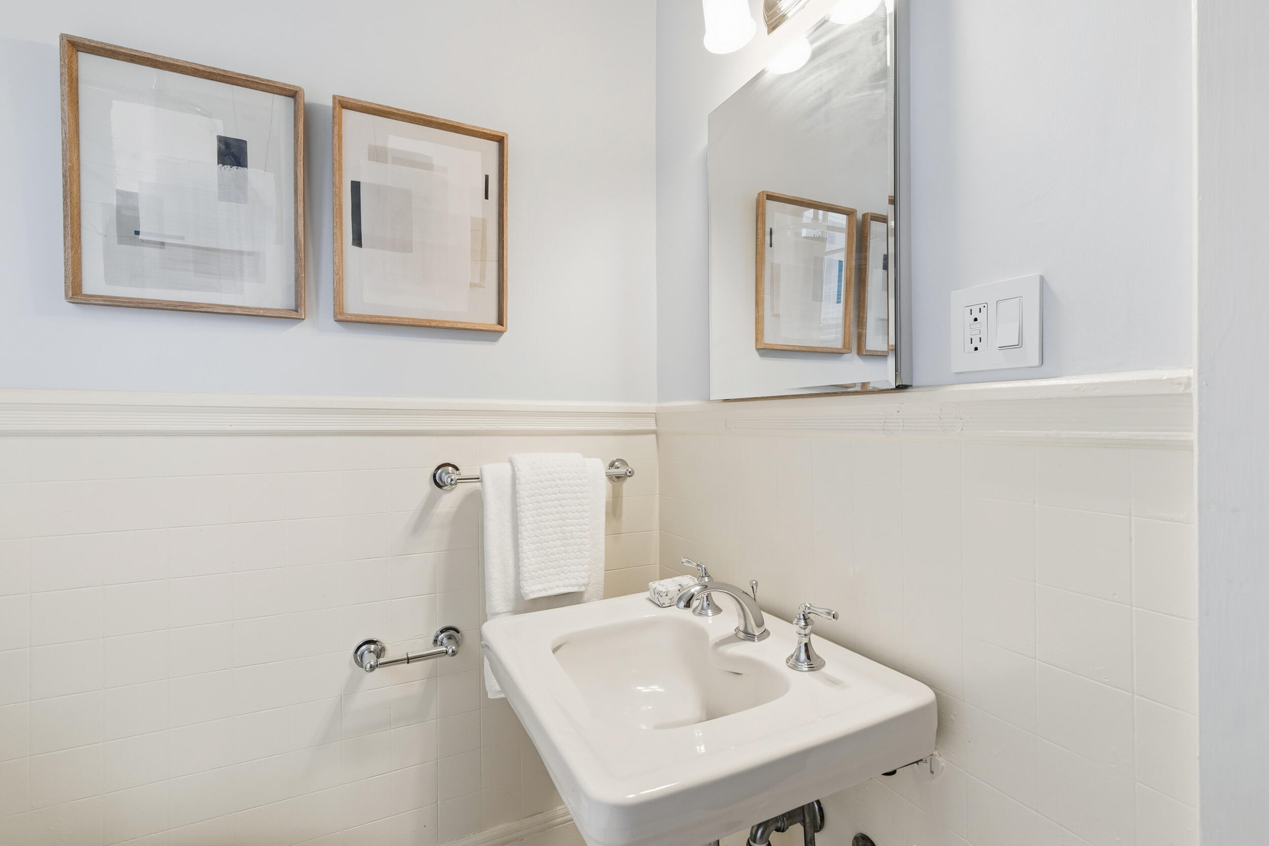 Bathroom vanity with a white sink, chrome fixtures, framed artwork, and a large mirror.