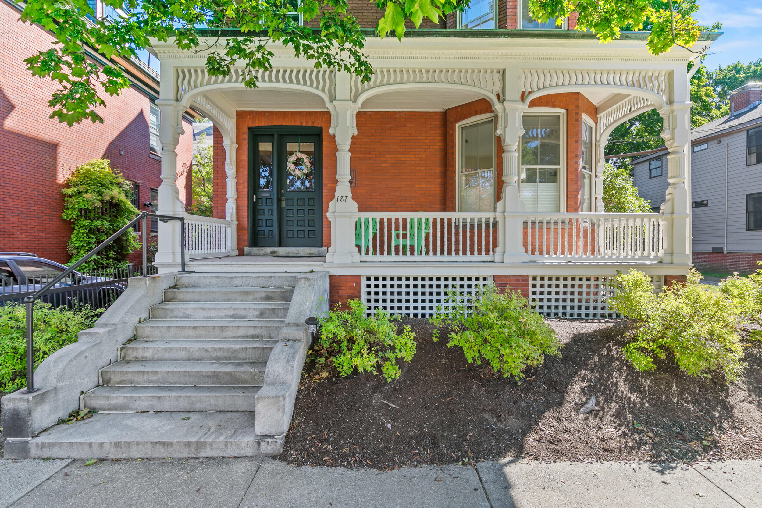 Red-brick home with an ornate white porch, dark double doors, and broad concrete steps.
