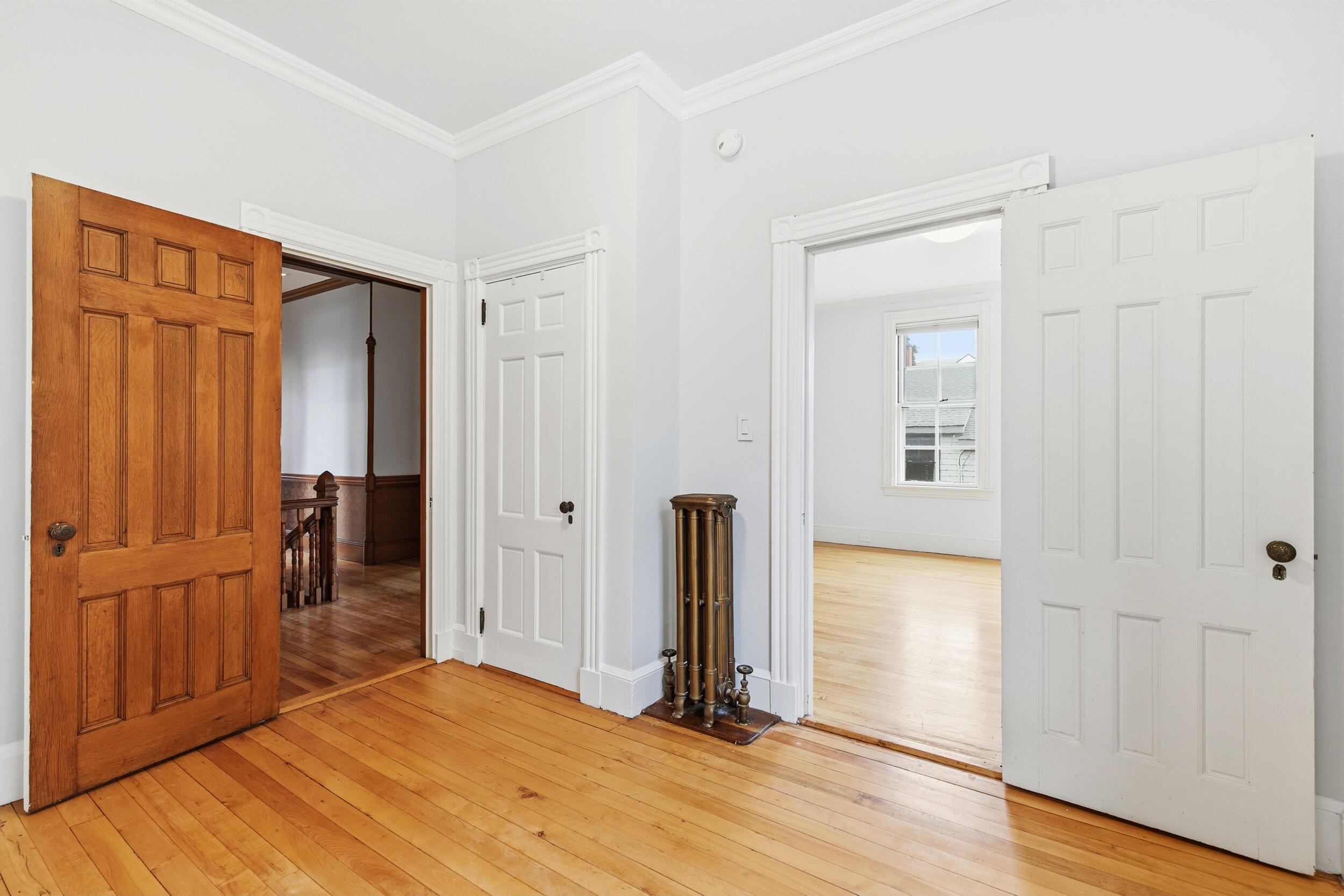 Bright hallway with hardwood floors, an ornate wooden door, and a vintage radiator between open doorways.