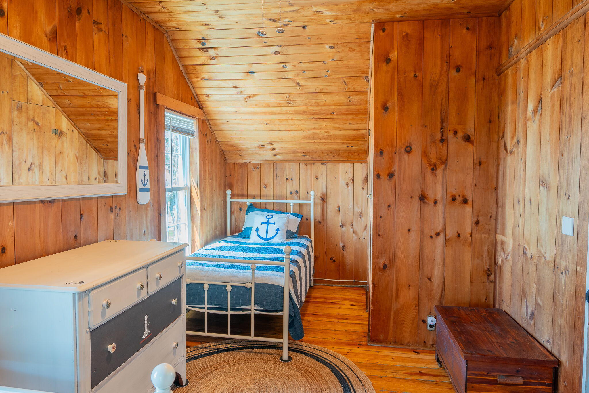 Single bedroom with knotty pine walls, sloped wood ceiling, and a blue-and-white nautical bed.
