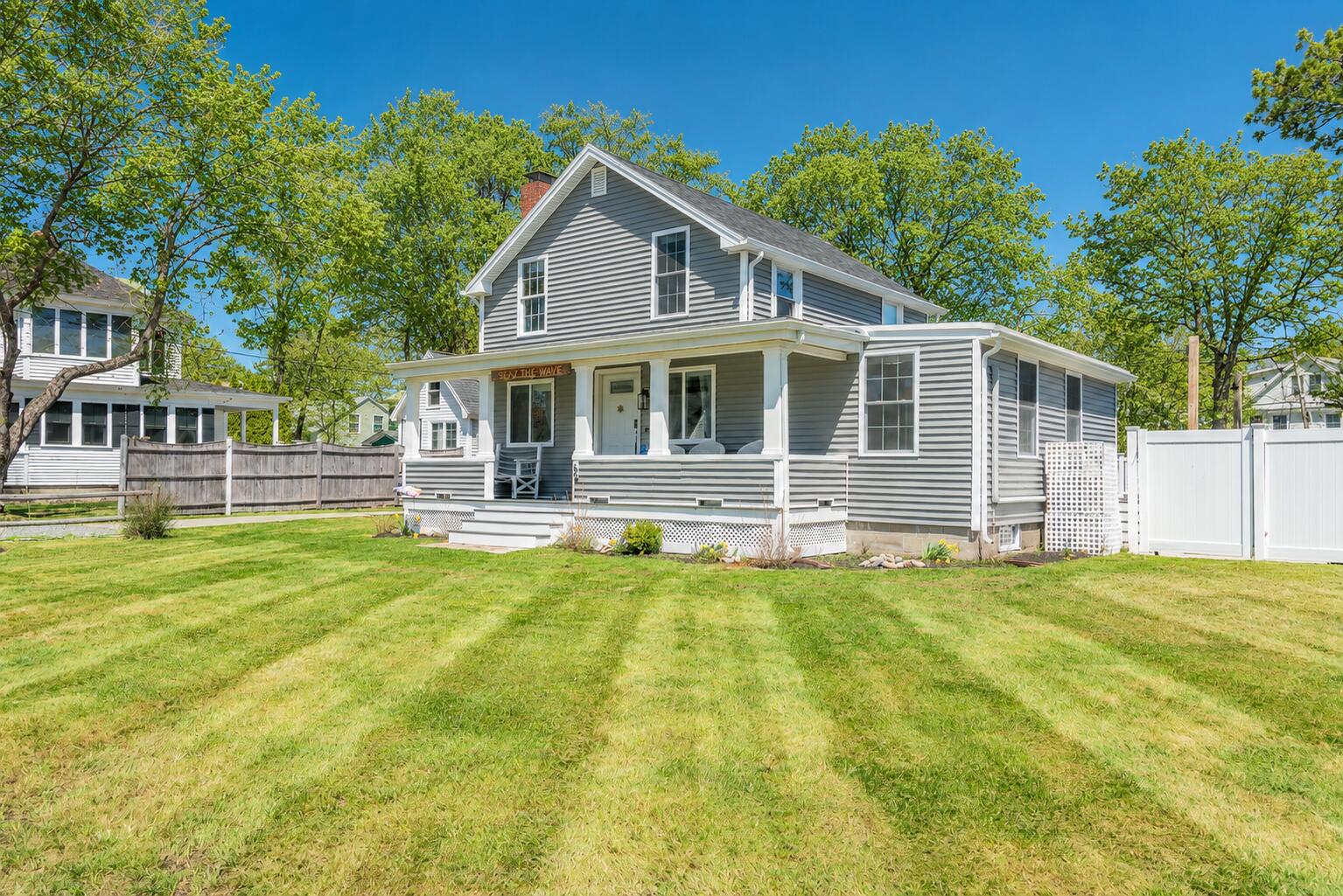 Gray two-story house with a broad covered porch, white fence, and freshly mown lawn.