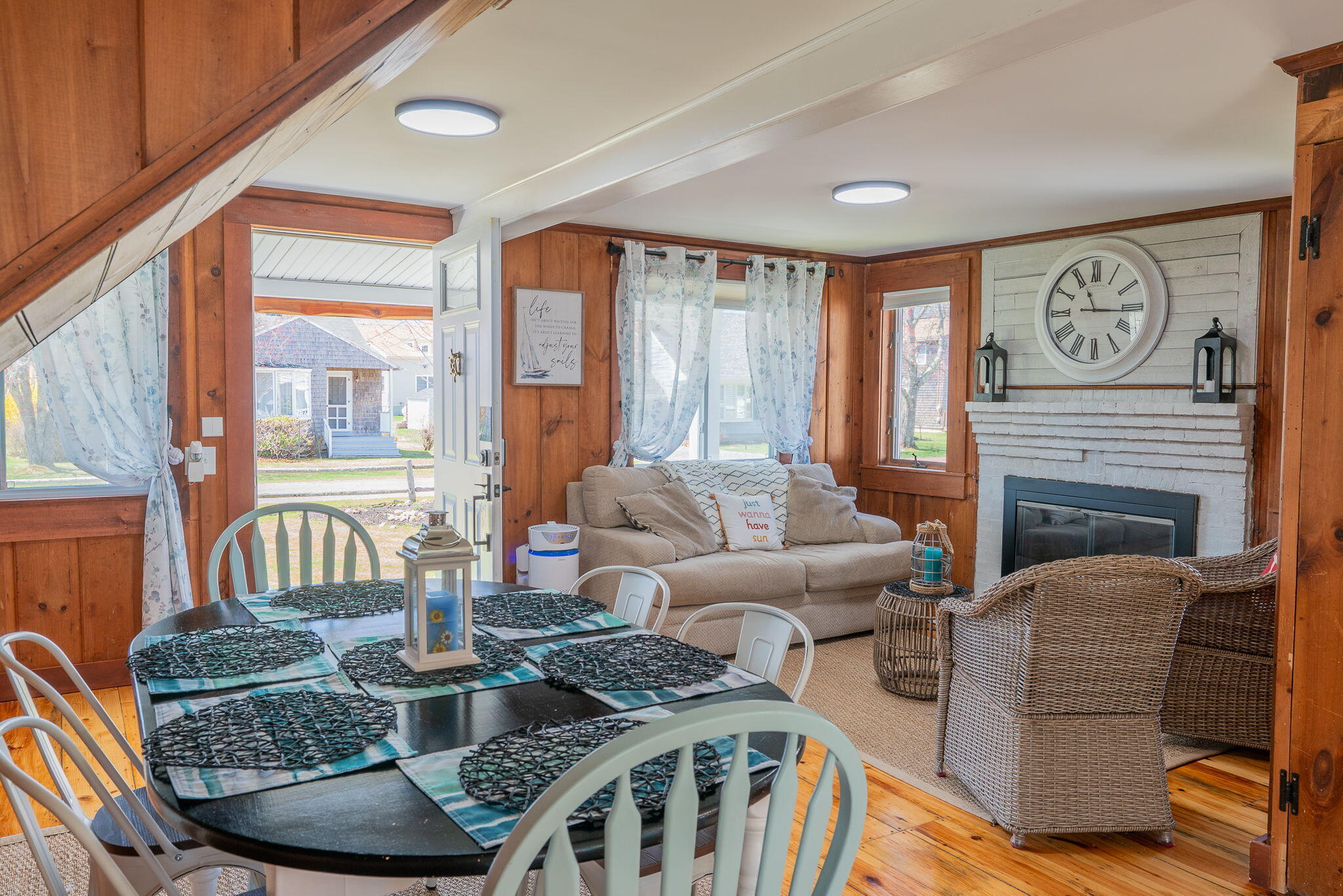 Living and dining room with wood-paneled walls, a white brick fireplace, and a set dining table.